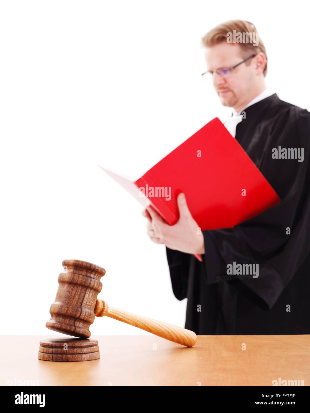 Wooden justice gavel in focus, blurry judge in background, reading big red book Stock Photo