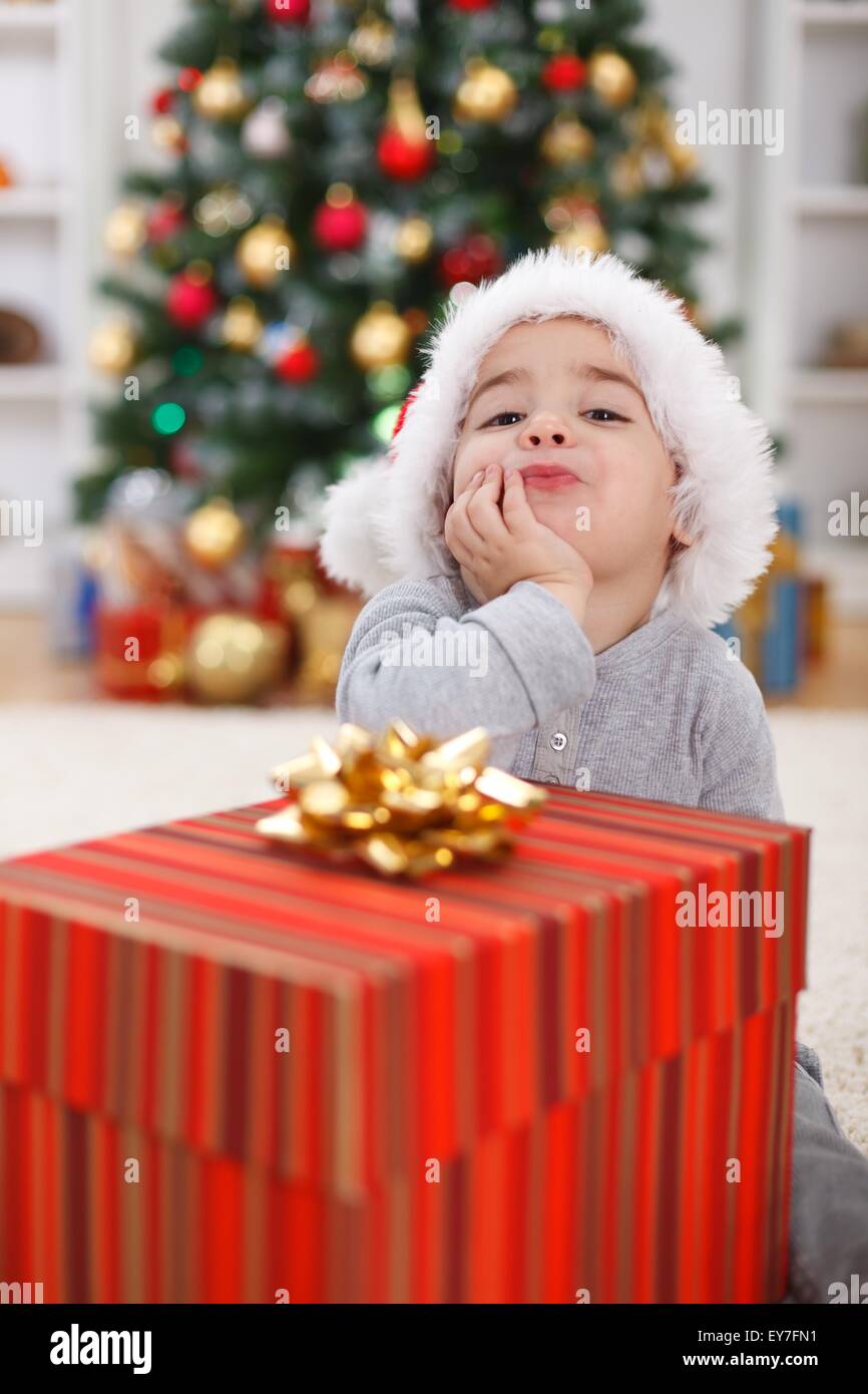 Cute little boy with big present, sitting in front of Christmas tree Stock Photo