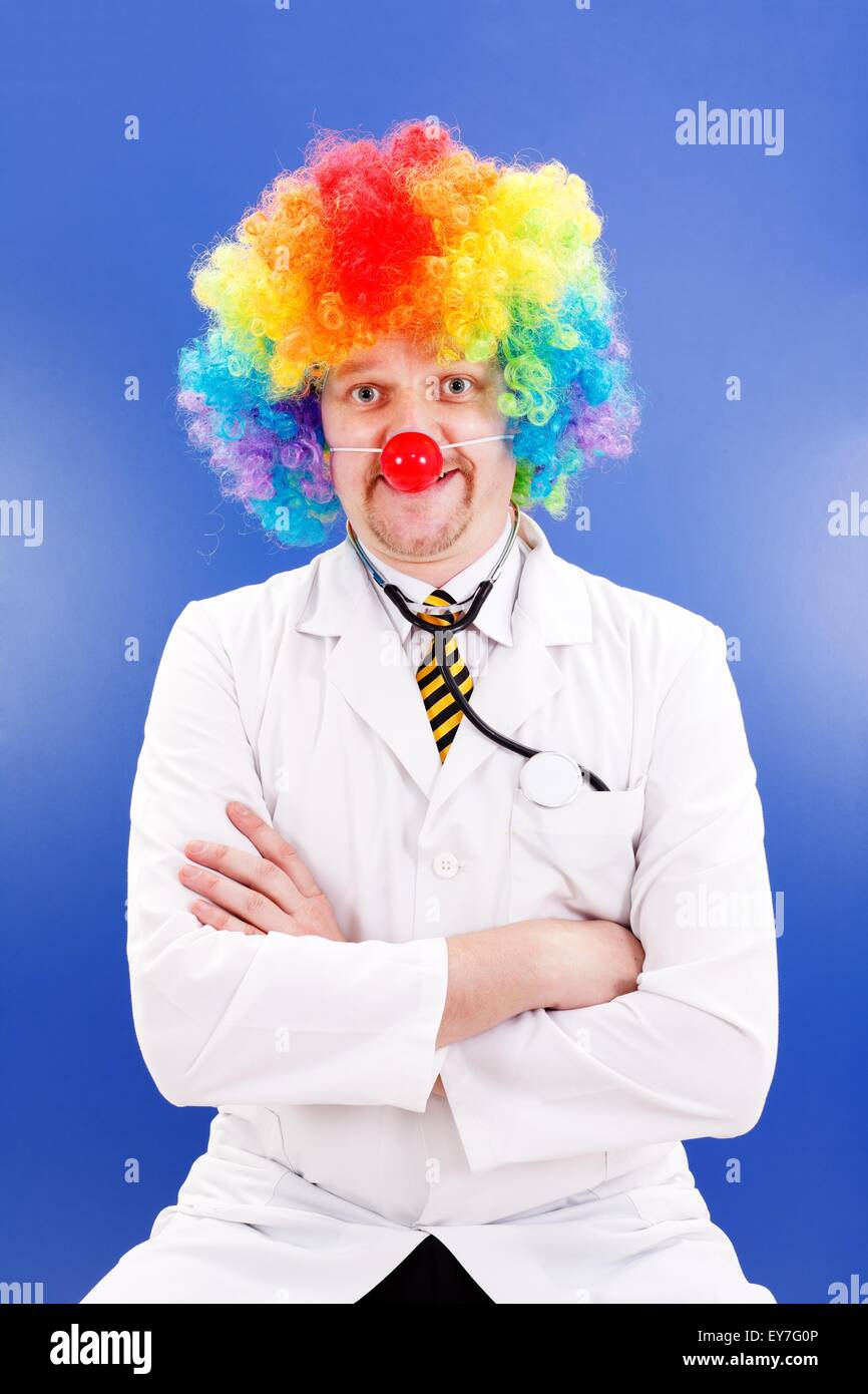 Funny clown doctor on blue, wearing colorful wig and red ball nose Stock Photo