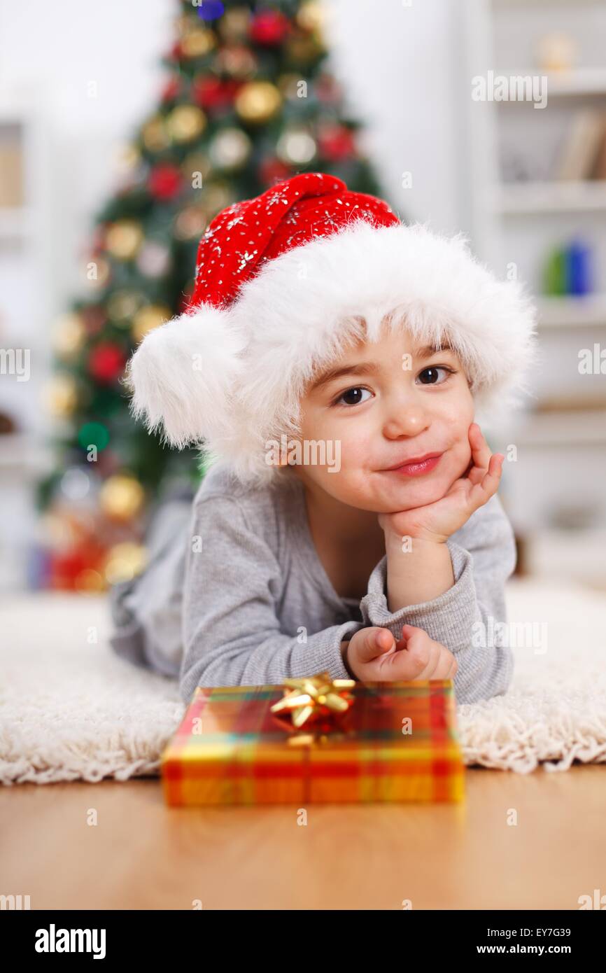 Little boy with present, prop his head, laying in front of Christmas