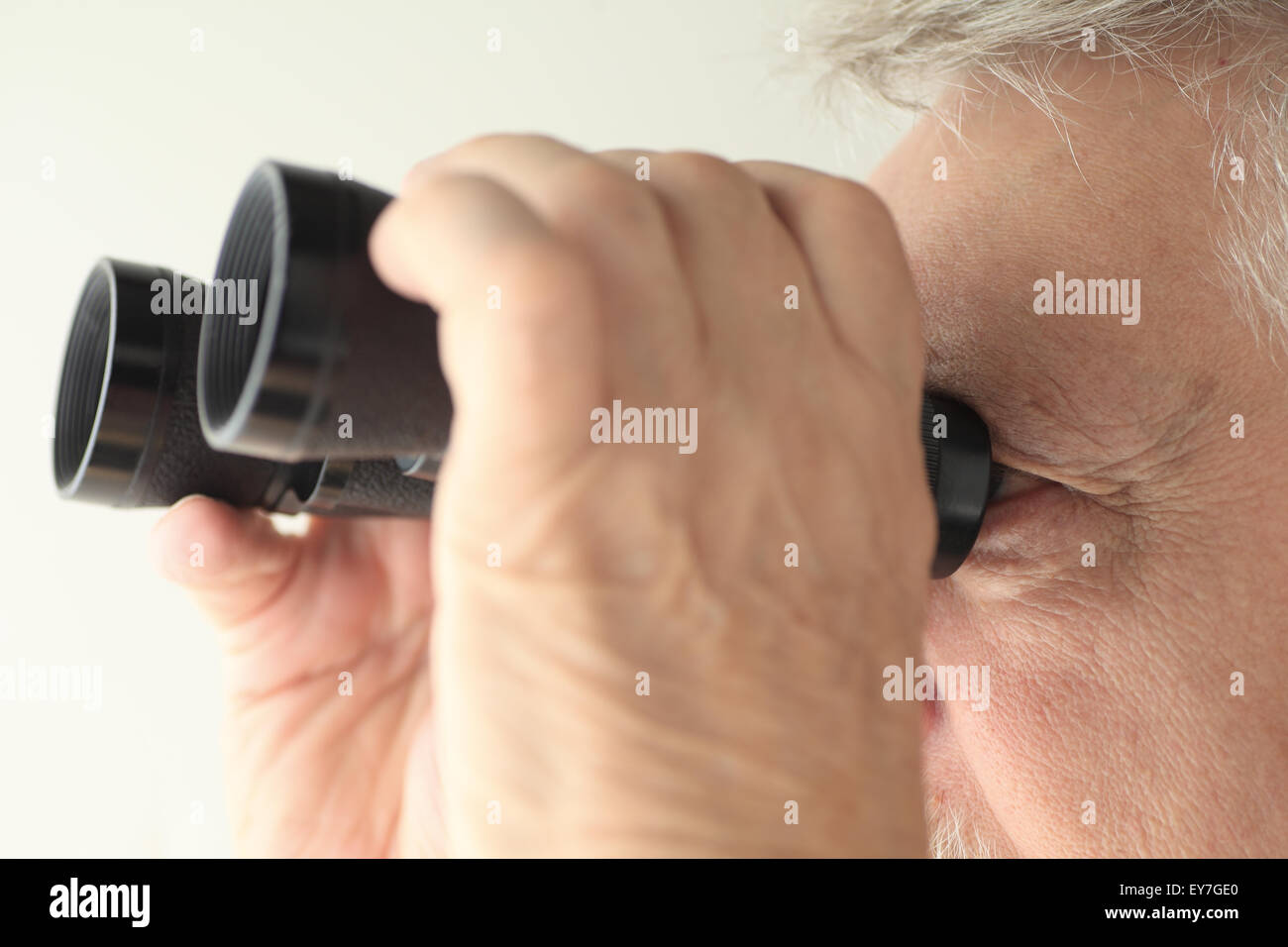 An older man looking through an old pair of binoculars Stock Photo