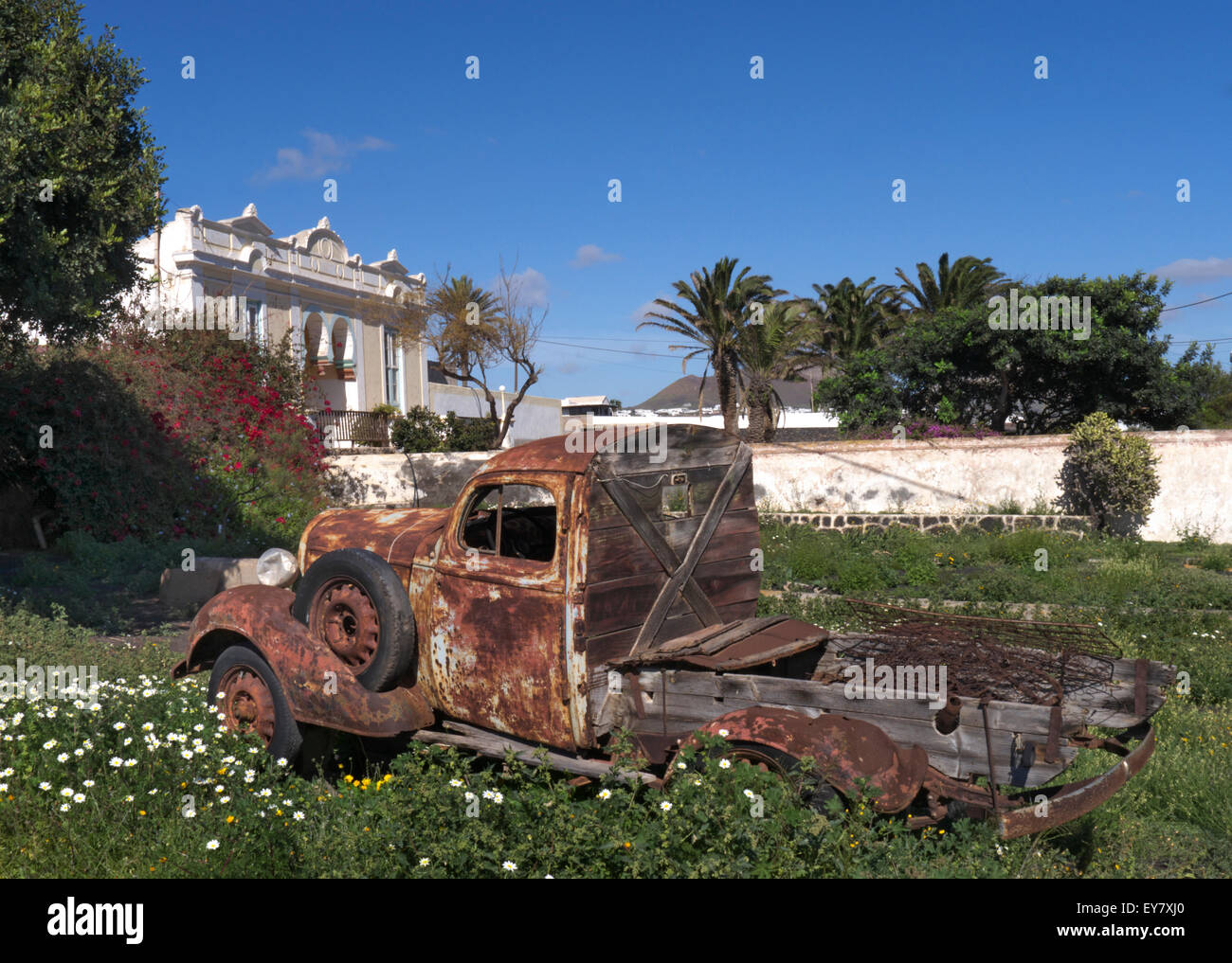 Rusting old pick up truck forms an attractive feature in a Lanzarote garden with old finca farm behind Canary Islands Spain Stock Photo