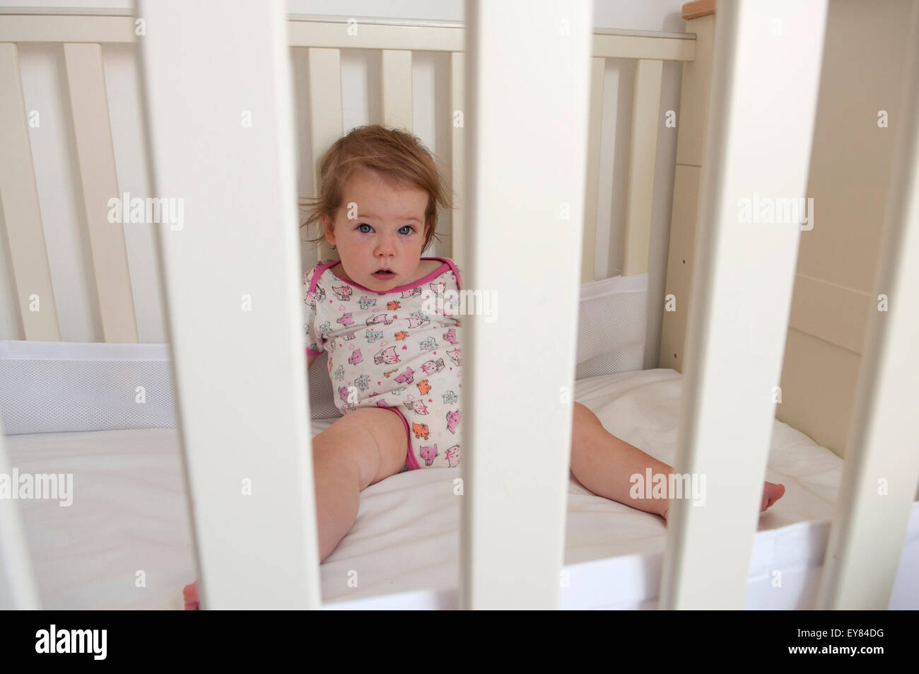 Baby girl looking through the bars of her cot looking apprehensive Stock Photo