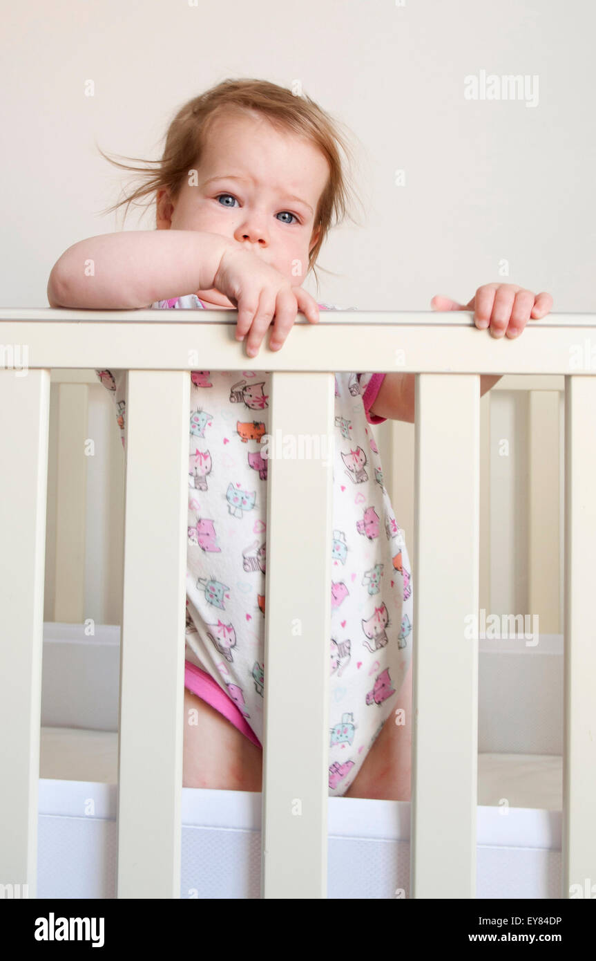 Baby girl looking over the bars of her cot looking apprehensive Stock Photo