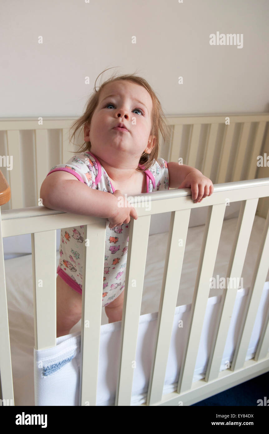 Baby girl looking over the bars of her cot Stock Photo