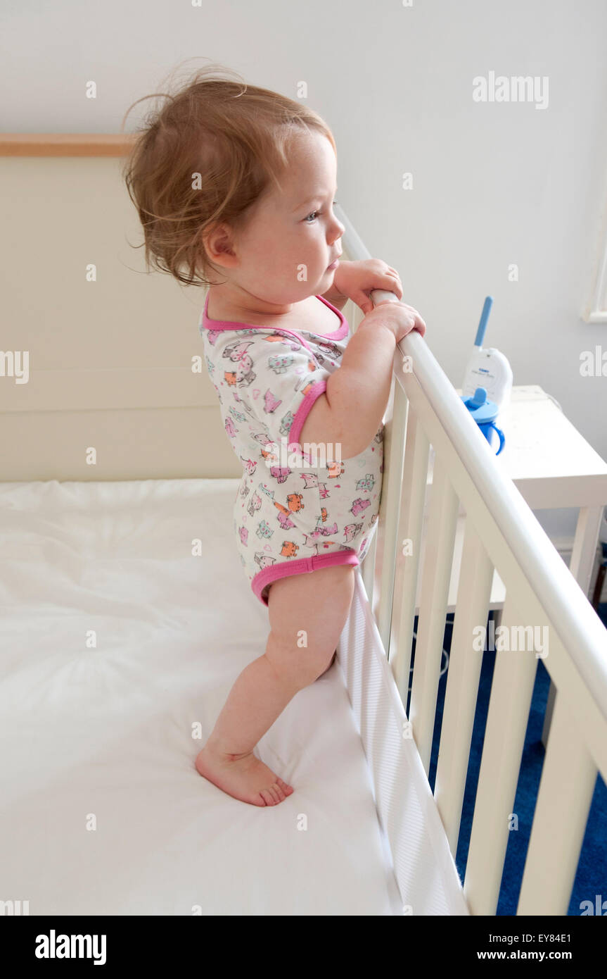 Side view shot of baby girl standing inside her cot looking inquisitive Stock Photo