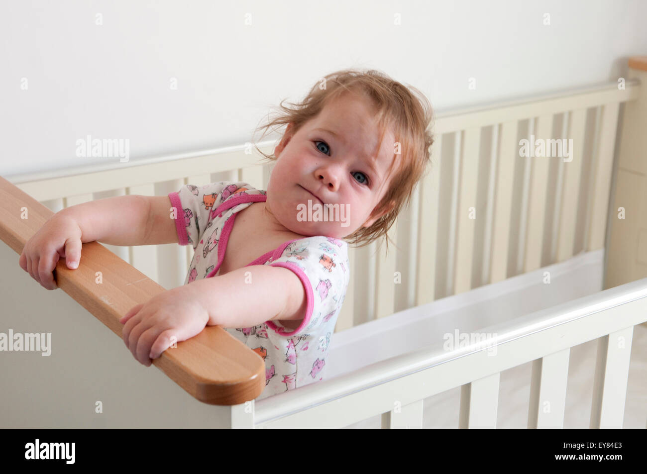 Baby girl standing inside her cot looking mischievous Stock Photo
