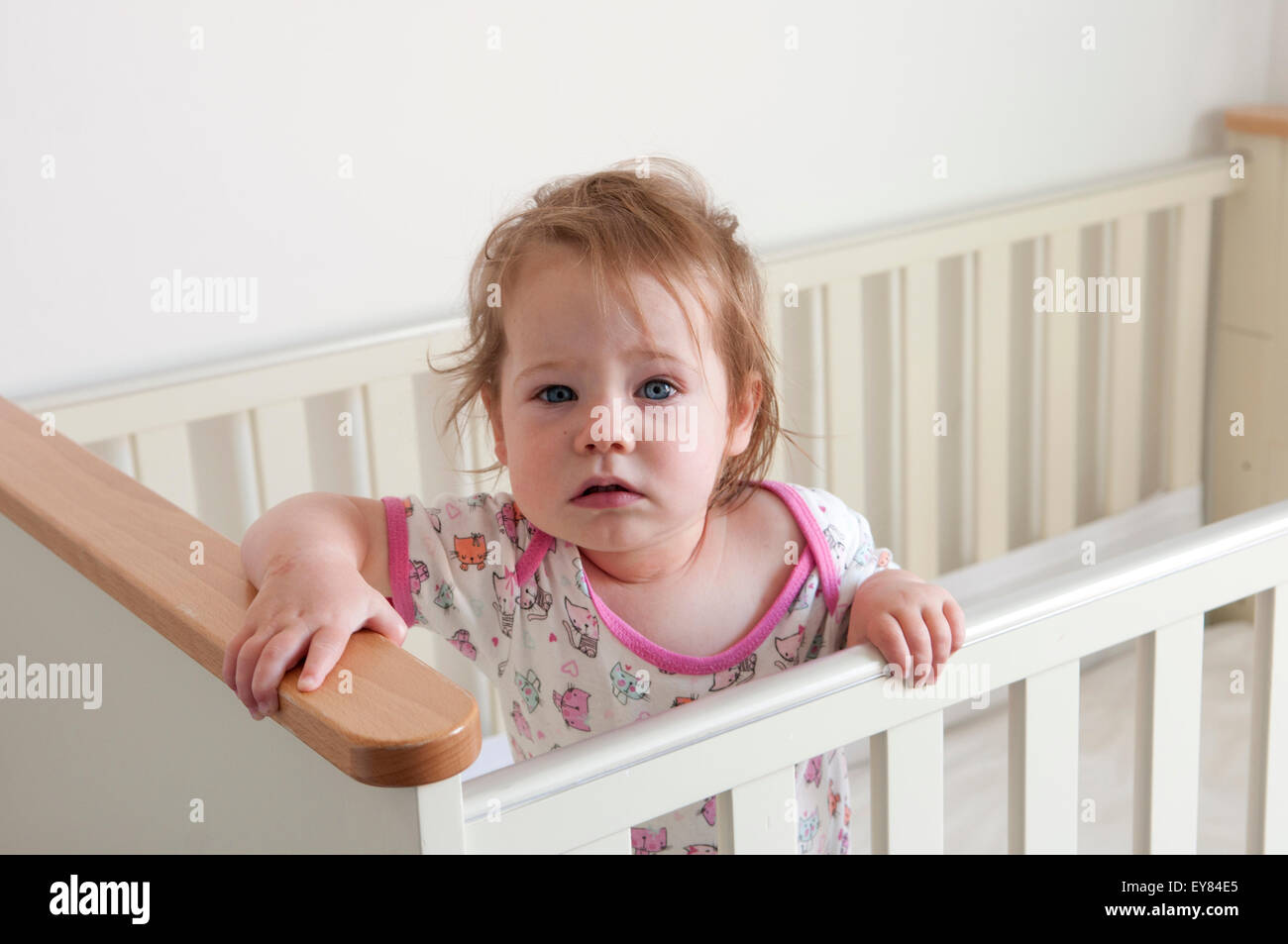 Baby girl standing inside her cot looking apprehensive Stock Photo