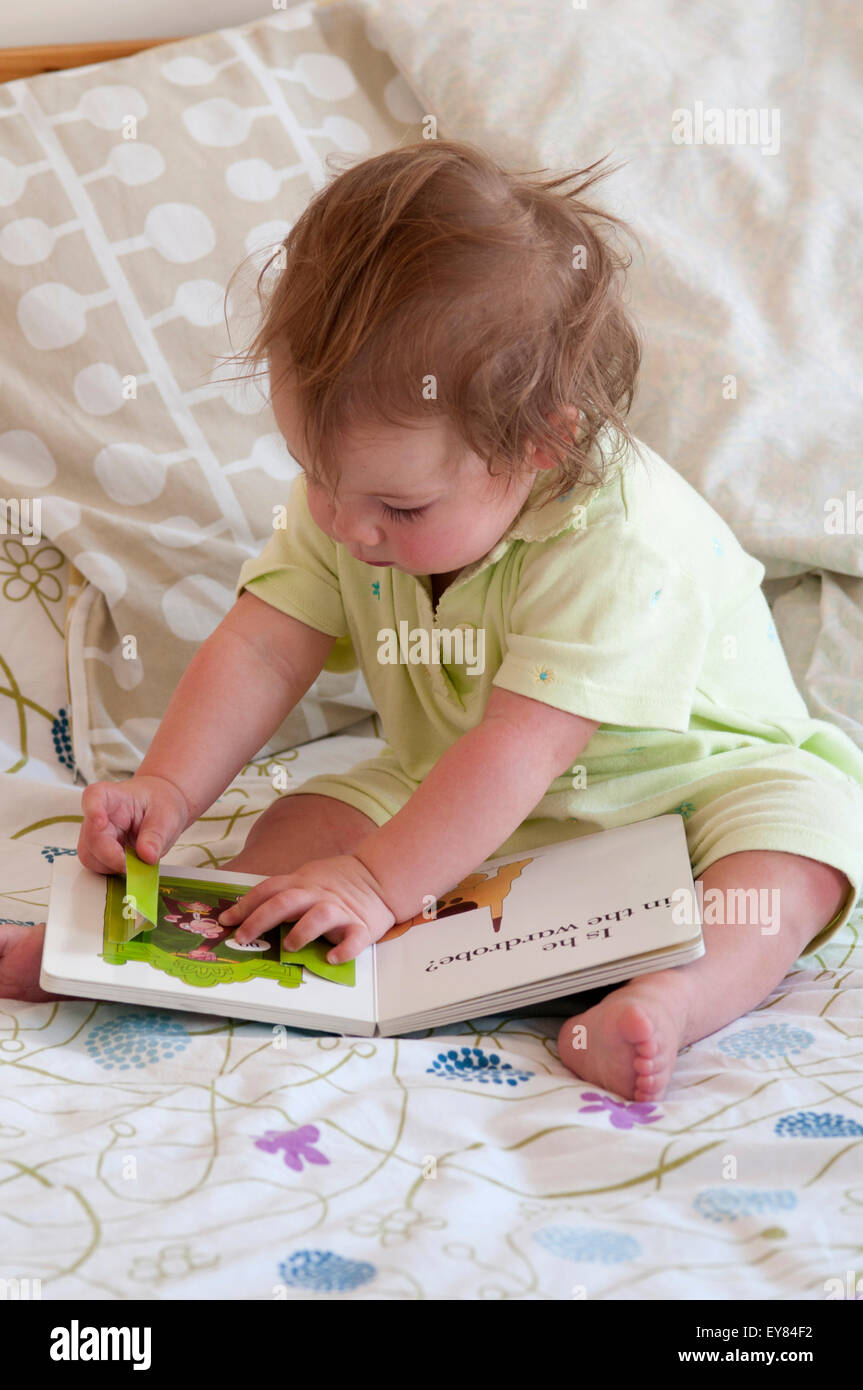 Baby girl sitting on the bed looking at a book Stock Photo - Alamy