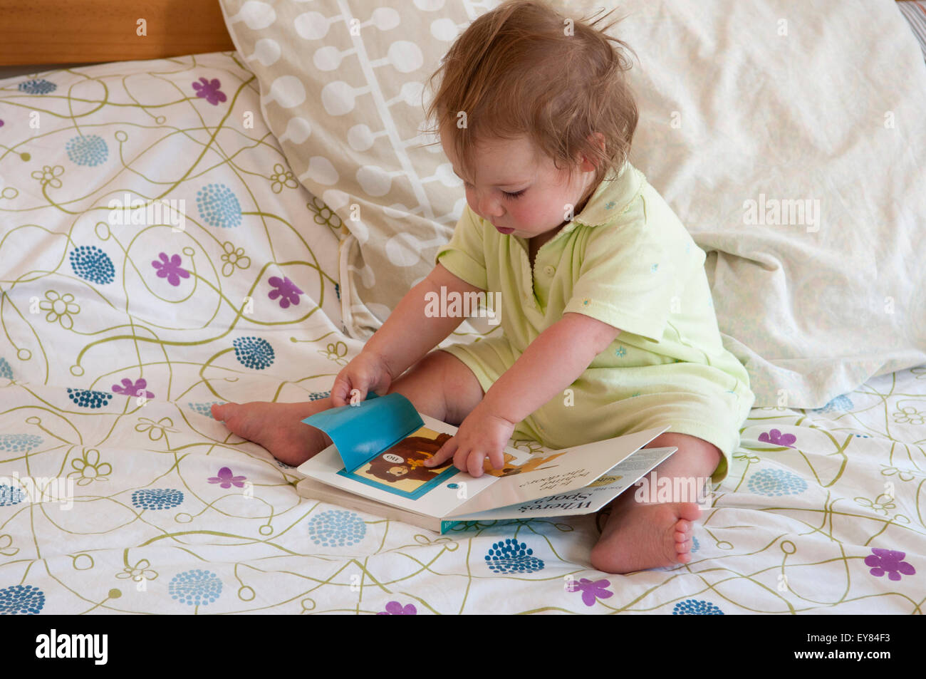 Baby girl sitting on the bed, looking at a book pointing Stock Photo ...