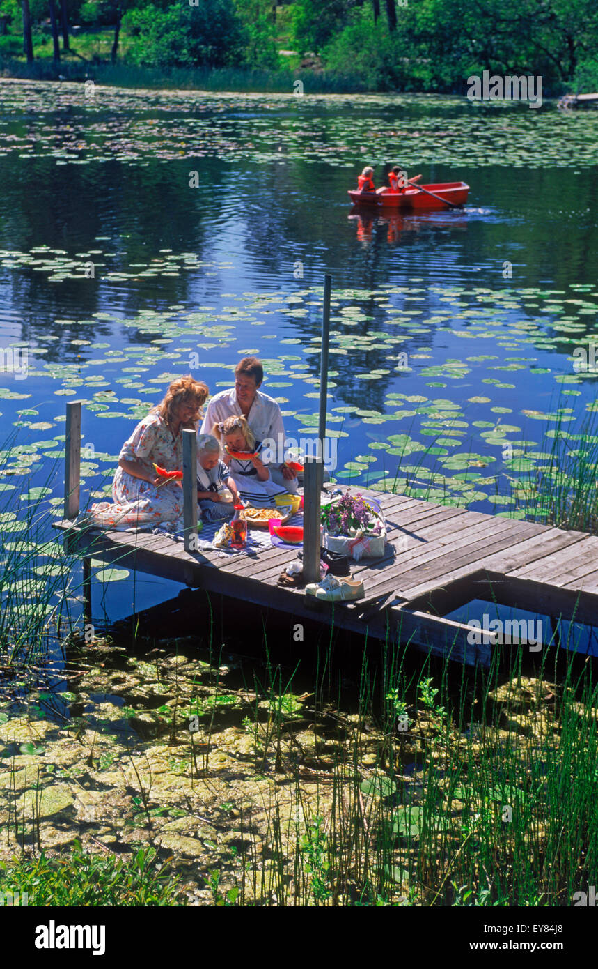 Family of four with picnic basket on lakeside pier during Swedish summer Stock Photo