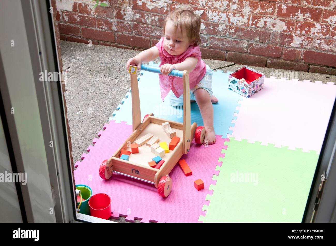 Baby girl pulling herself up on a baby walker Stock Photo Alamy