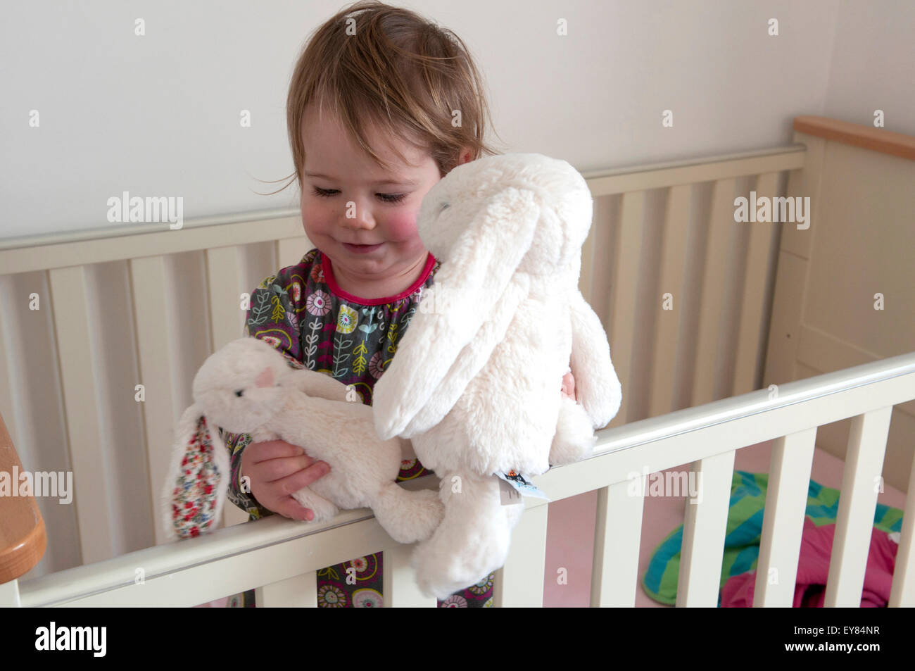 Happy little girl standing in her cot playing with soft toys Stock Photo