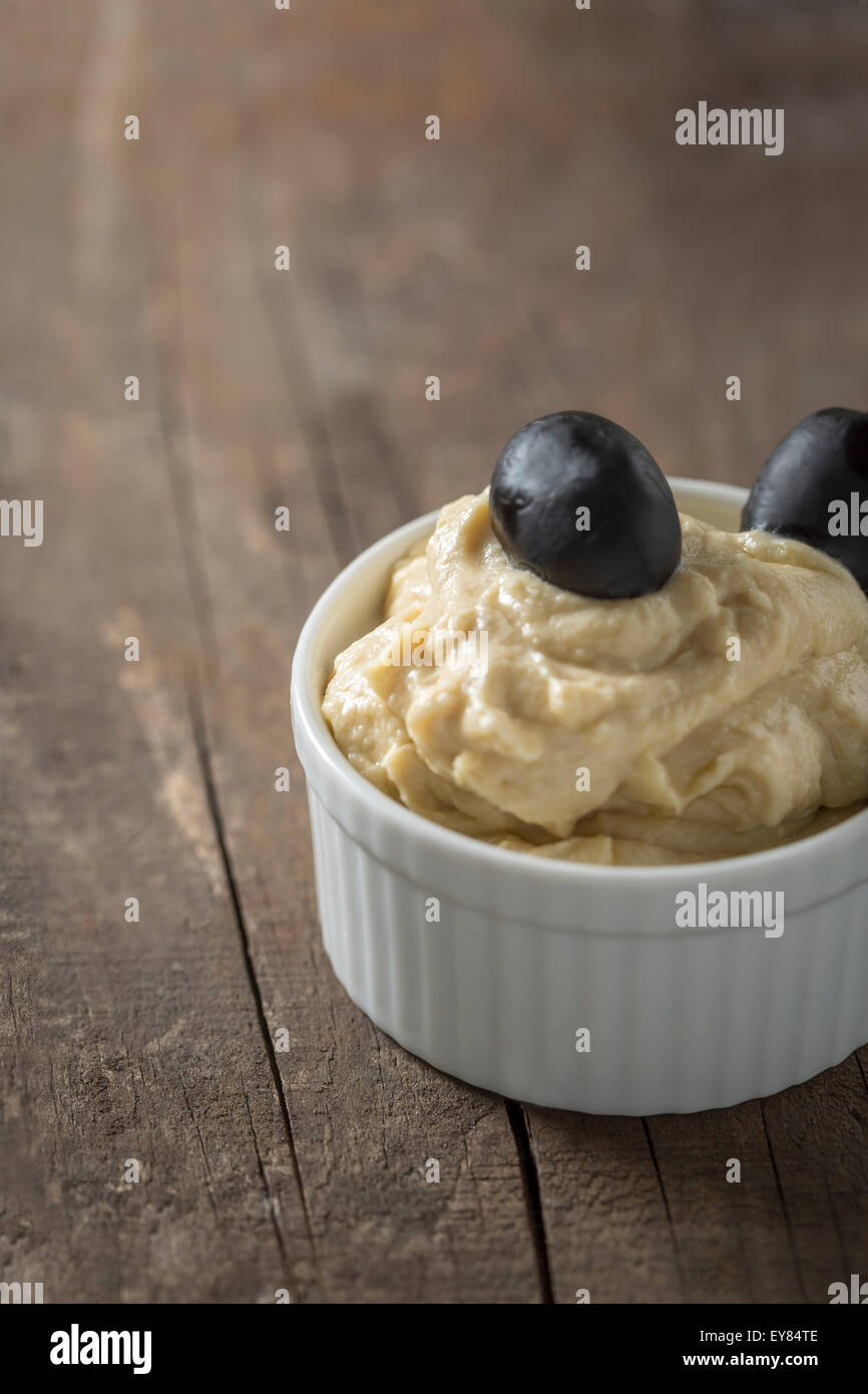Creamy Hummus with olives in a small bowl on wooden table Stock Photo