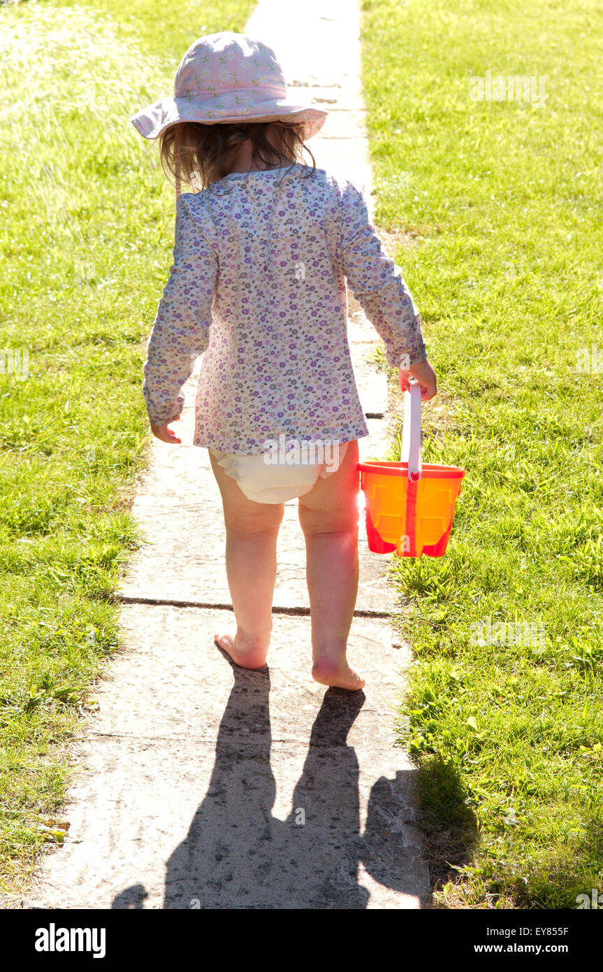 Rear view of a little girl walking up a garden path carrying orange bucket Stock Photo