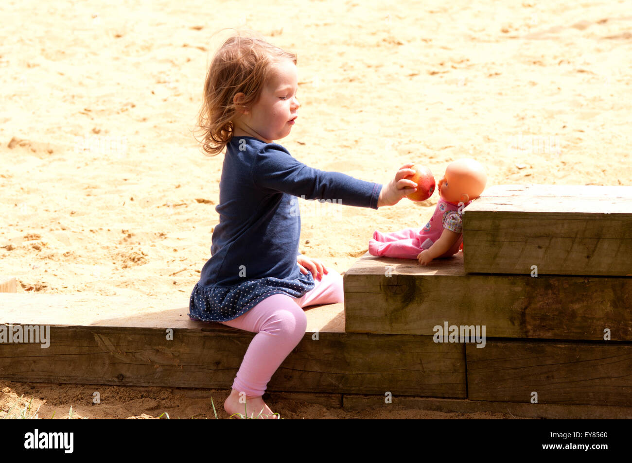 Little girl pretending to feed her doll with an apple Stock Photo