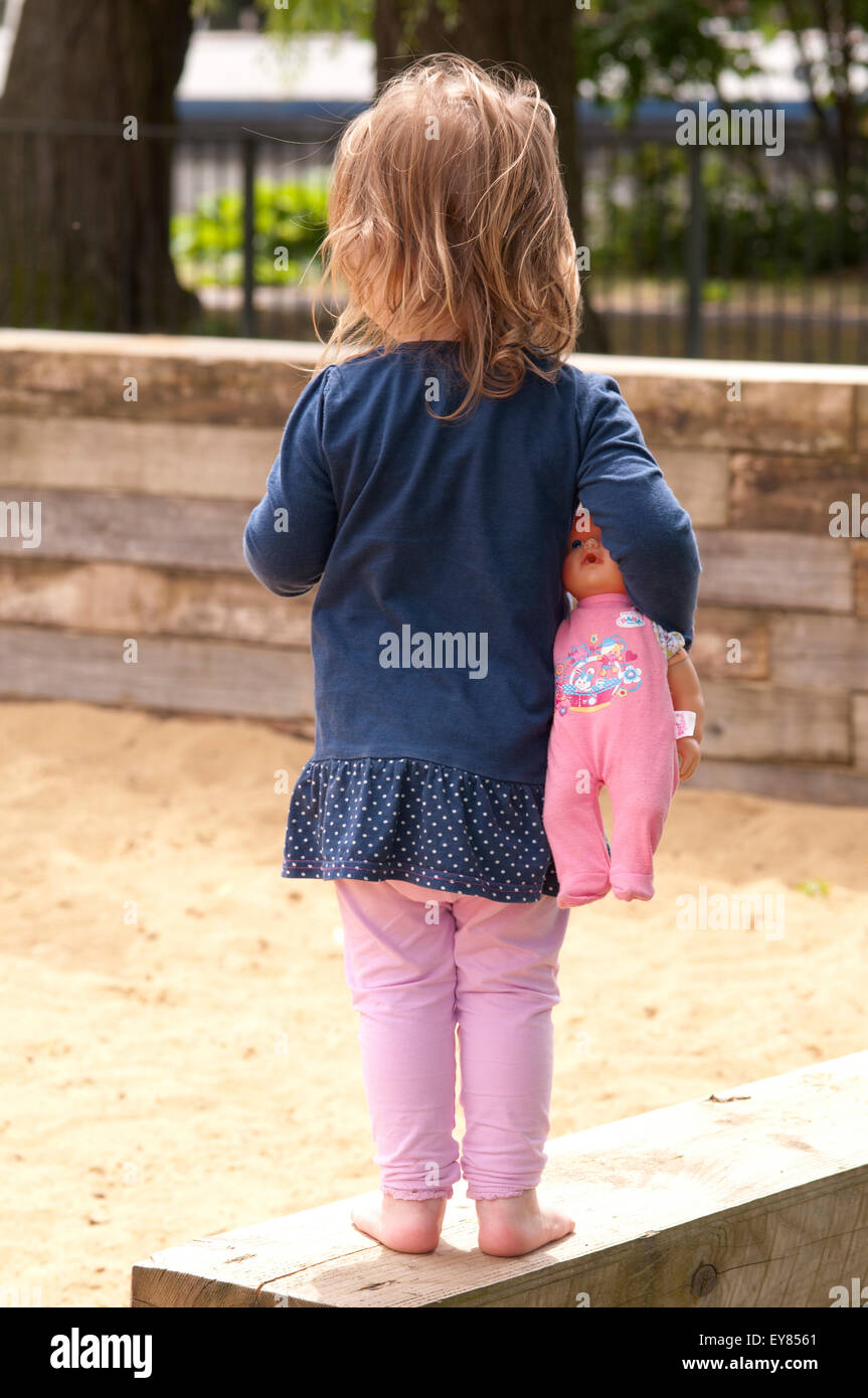 Rear view of a little girl standing carrying her doll Stock Photo Alamy