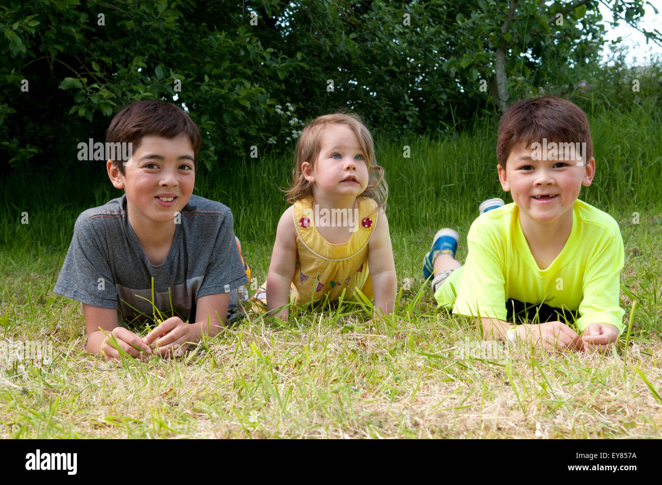 Little girl lying on the grass with two boys Stock Photo