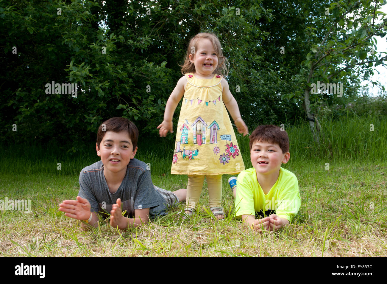 Little girl laughing, standing between two boys who are lying on their fronts Stock Photo