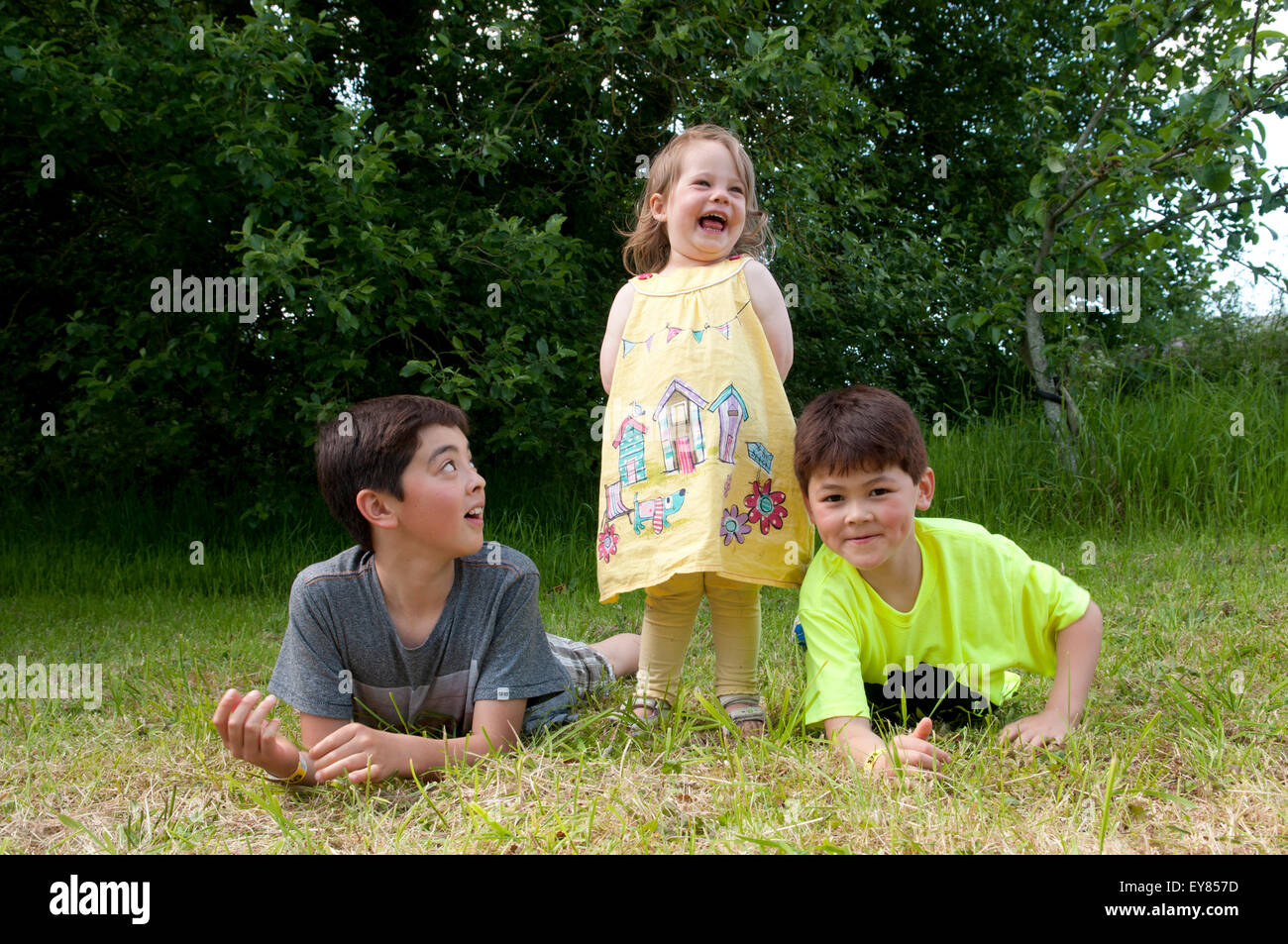 Little girl laughing, standing between two boys who are lying on their fronts Stock Photo