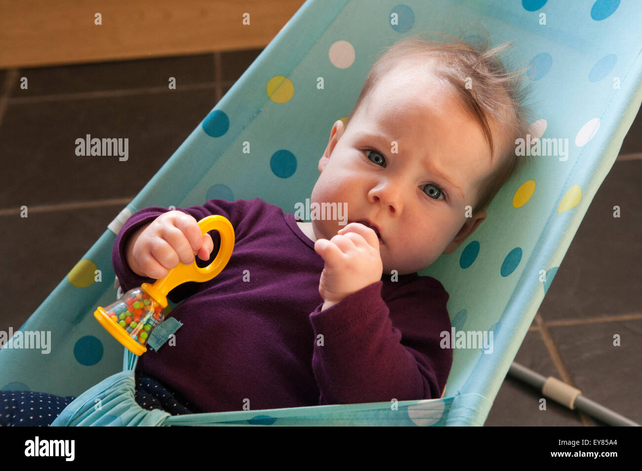 Portrait of little baby girl in a baby bouncer chewing her hand Stock Photo