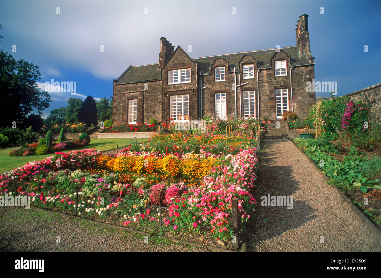 Estate house made of rocks at the Glendronach spirit distillery with garden flowers, stone walls and walkways in Scotland Stock Photo