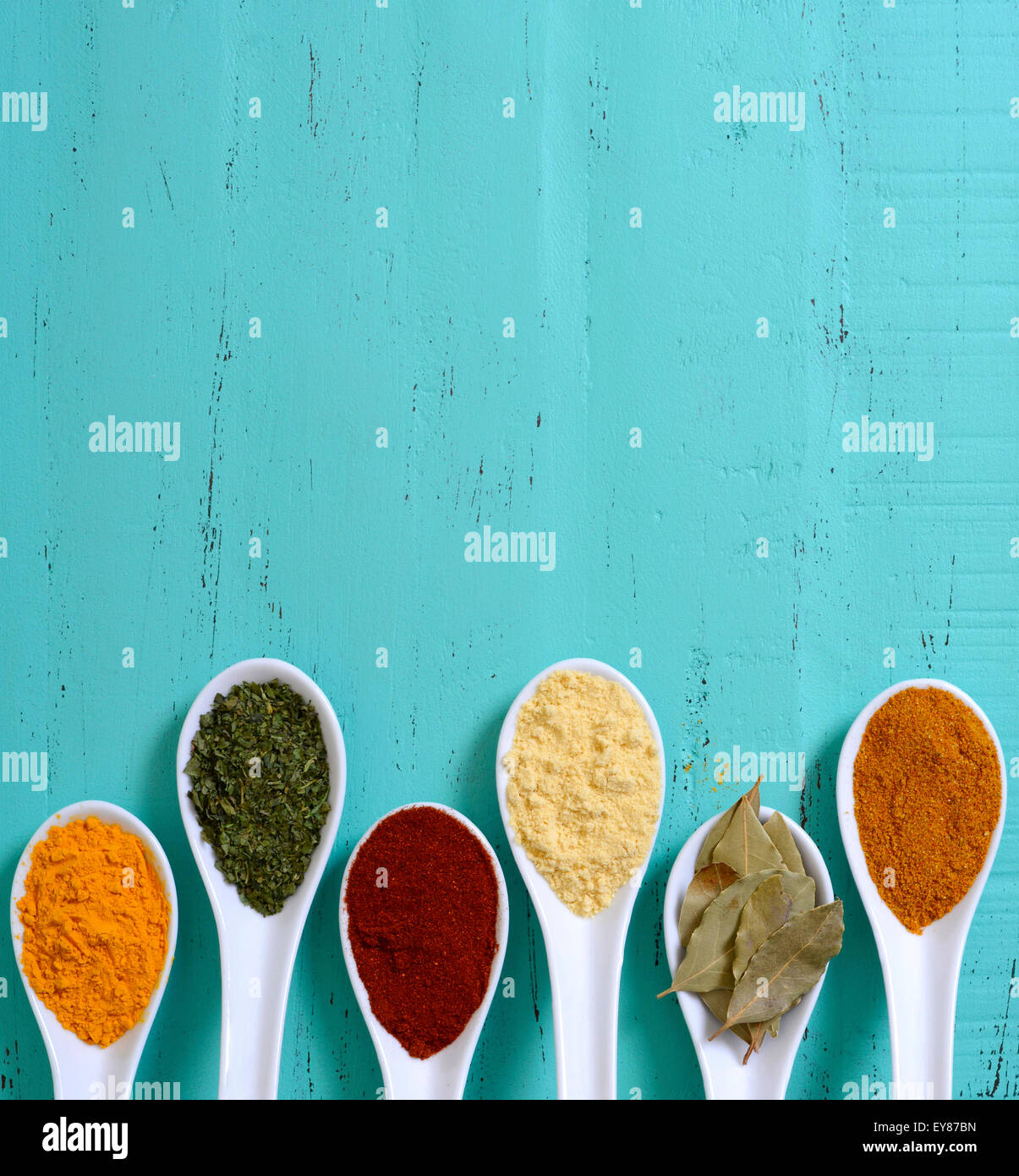 Colorful cooking spices and herbs in white spoons on vintage aqua blue table overhead with copyspace for your text here. Stock Photo