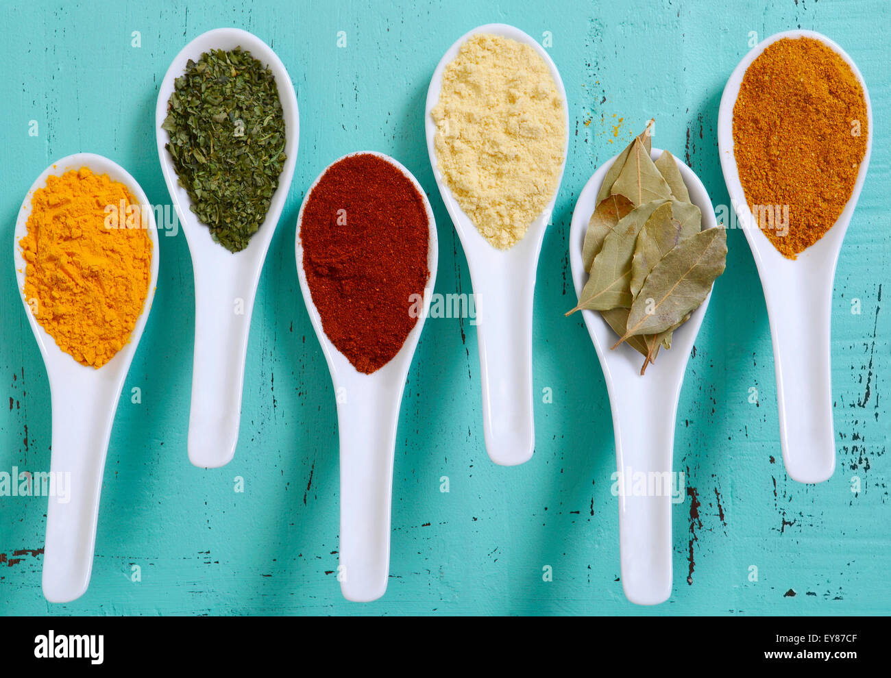 Colorful cooking spices and herbs in white spoons on vintage aqua blue table overhead. Stock Photo