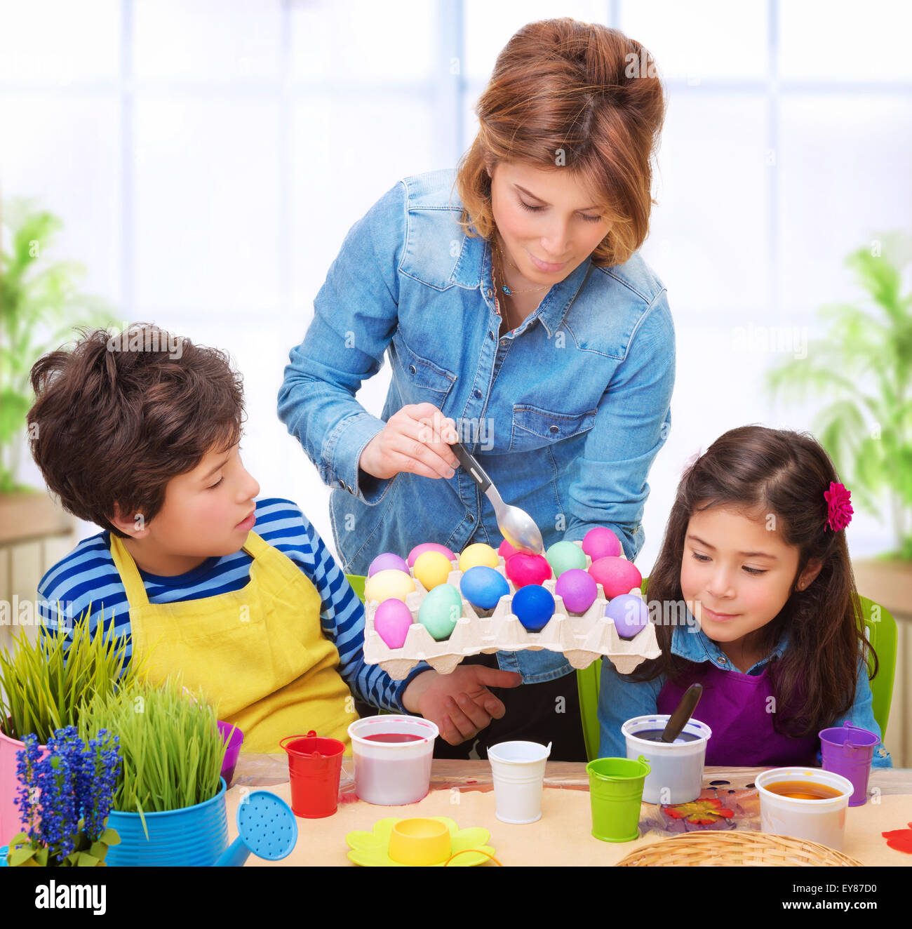 Happy family paint Easter eggs at home, mother showing her precious kids how to make traditional Easter decorative food Stock Photo
