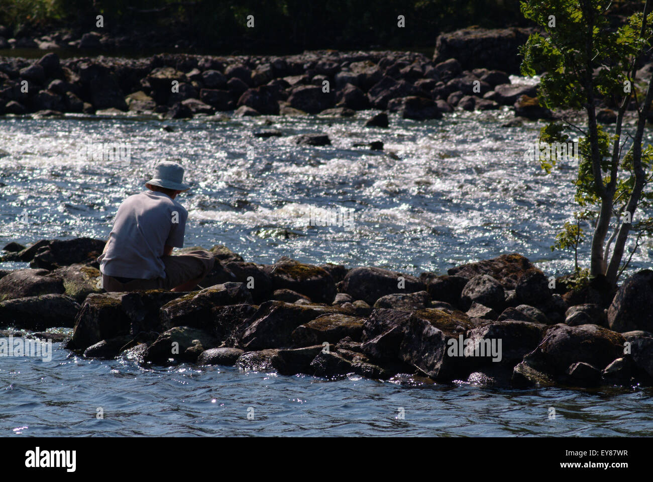 Rear view shot of teenage boy sitting on rocks by river Stock Photo - Alamy