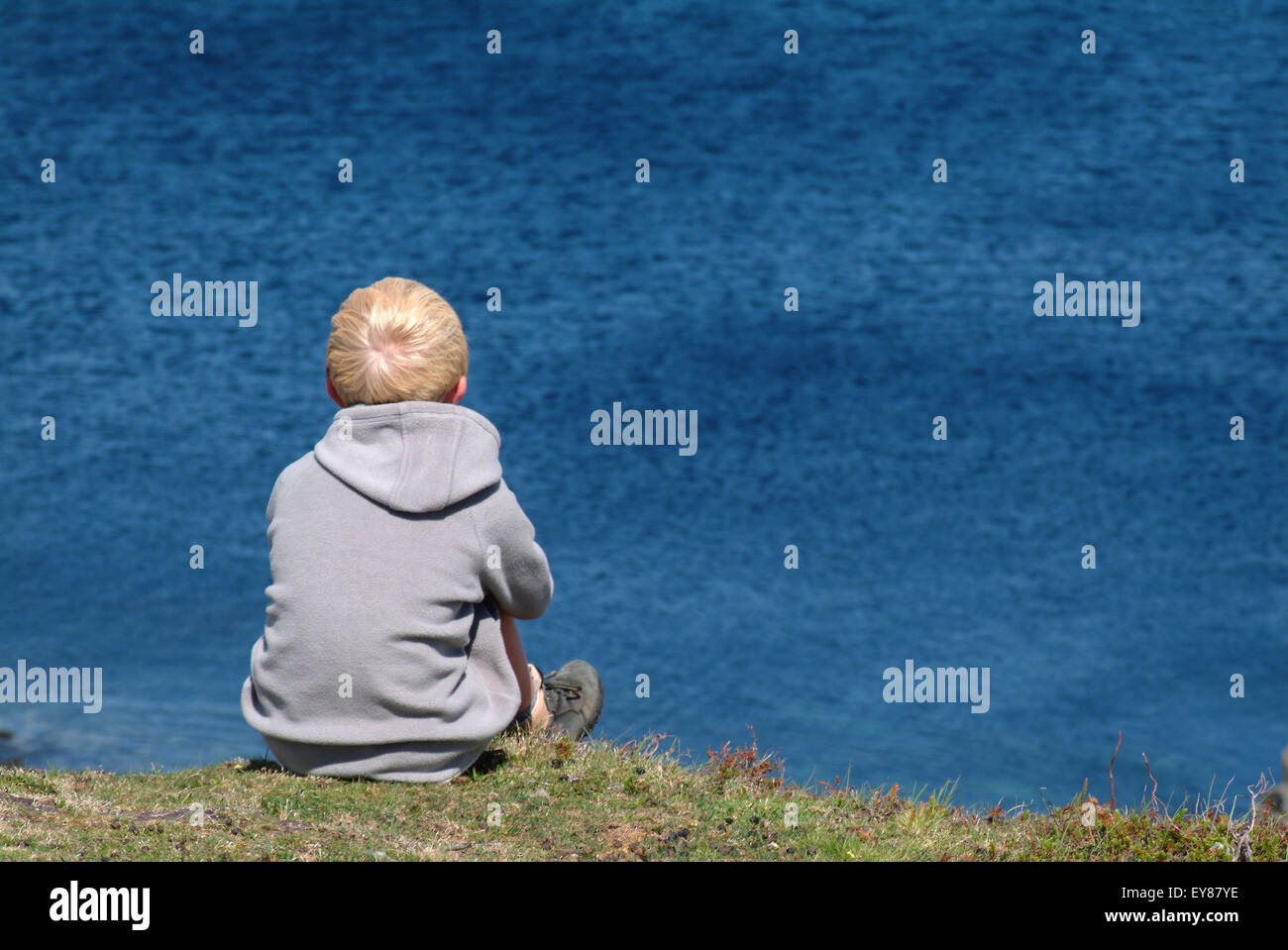 Rear view of young boy sitting on rocks looking out to sea Stock Photo ...