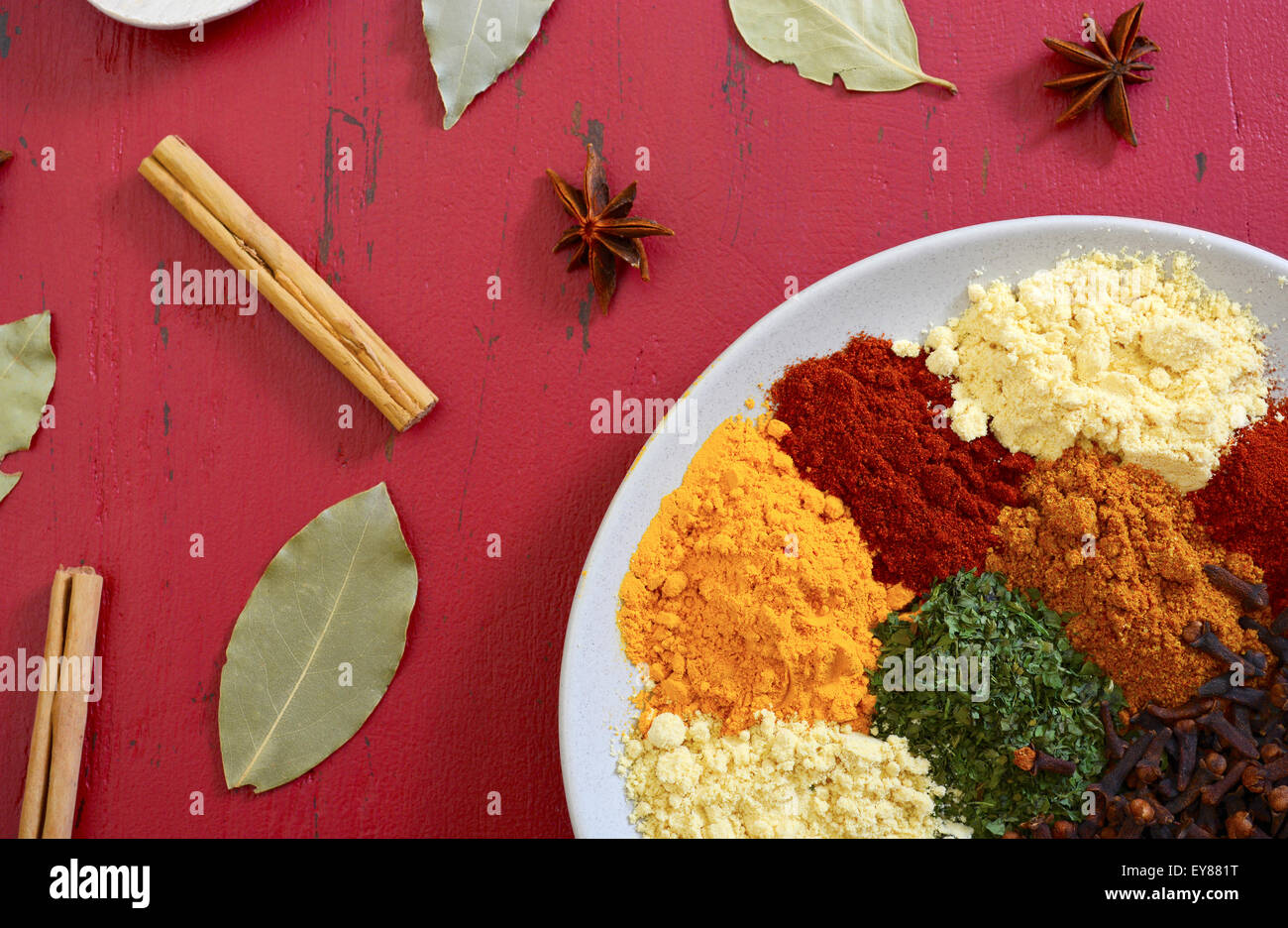 Colorful cooking spices and herbs overhead on vintage red wood table. Stock Photo