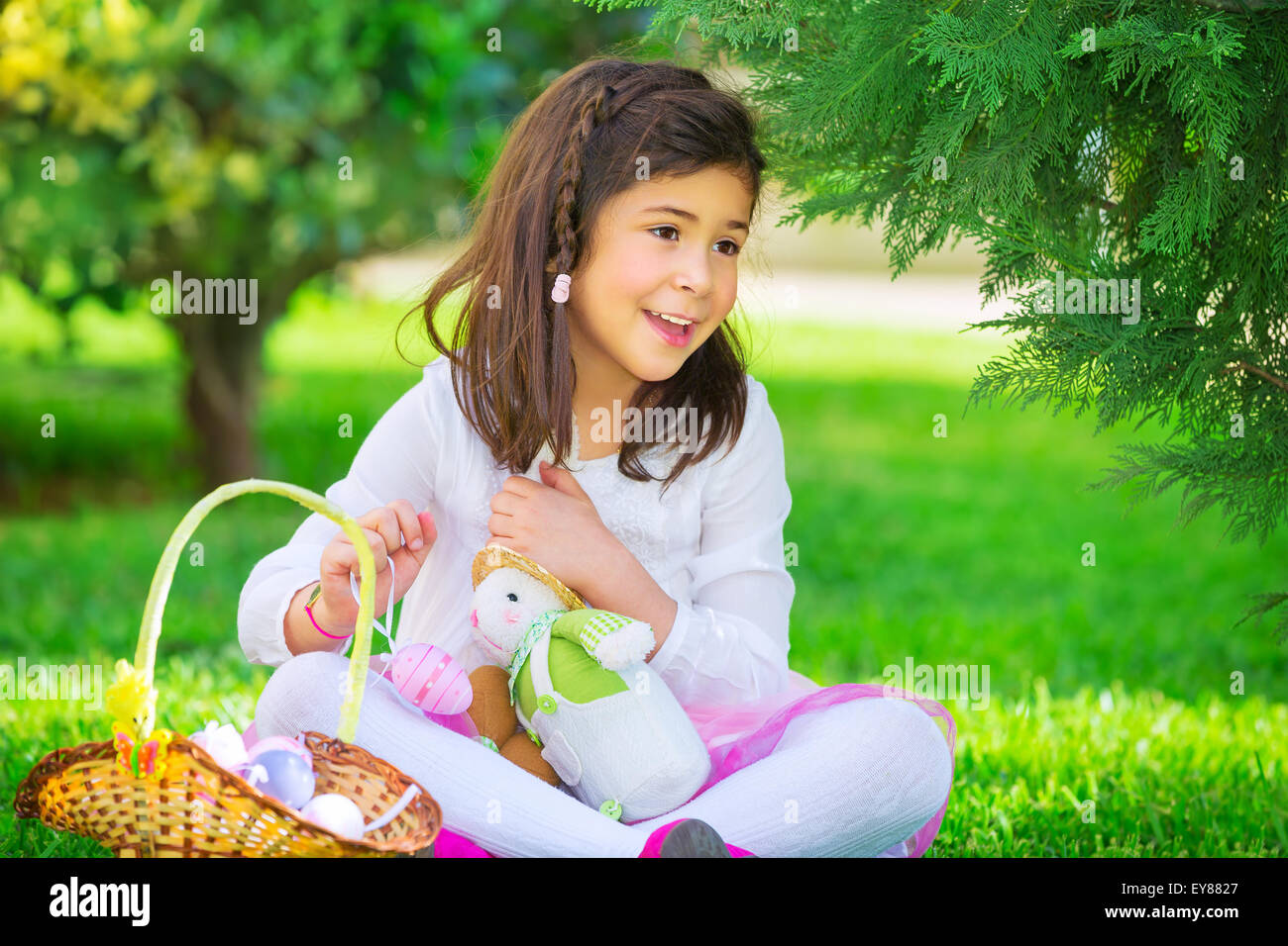 Little girl playing game outdoors with her rabbit toy, sweet adorable child finding colorful eggs, traditional Easter game Stock Photo