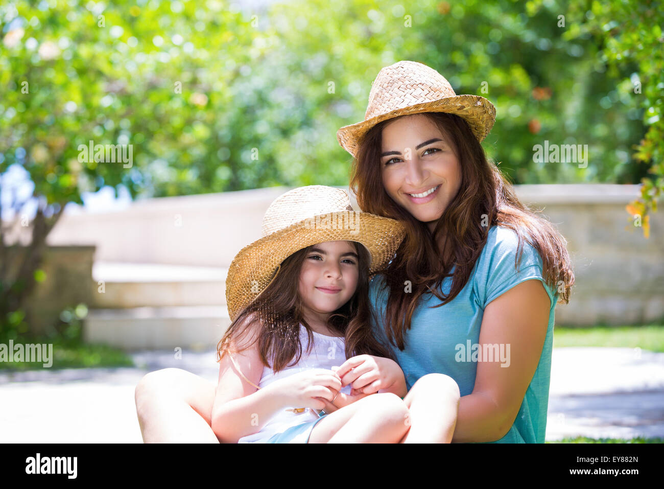 Happy family outdoors, cute cheerful mother with little daughter wearing identical straw hats and having fun on backyard Stock Photo