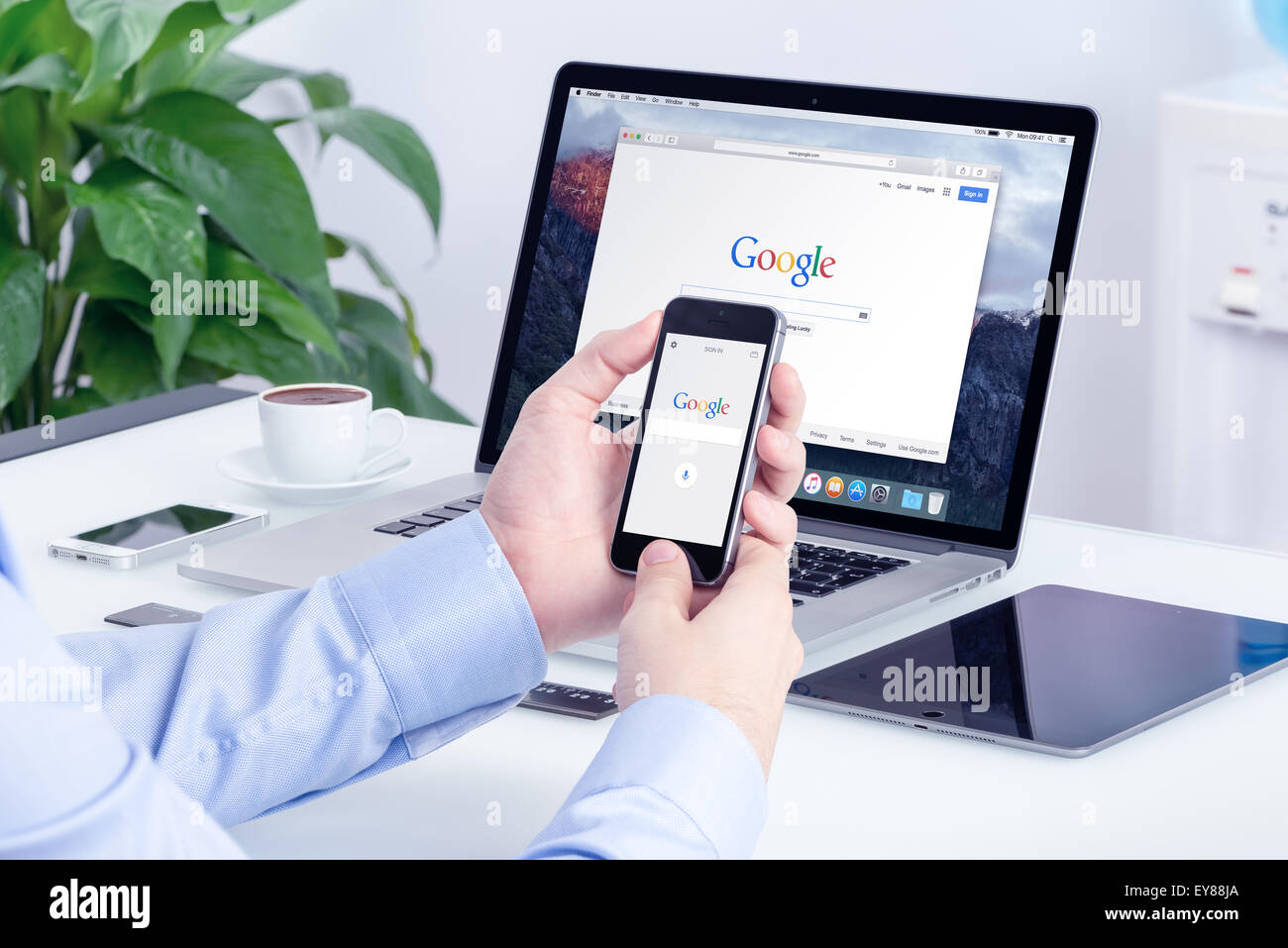 Google search on Apple iPhone screen and Macbook Pro Retina display that is on office desk. Multi devices multitasking concept. Stock Photo