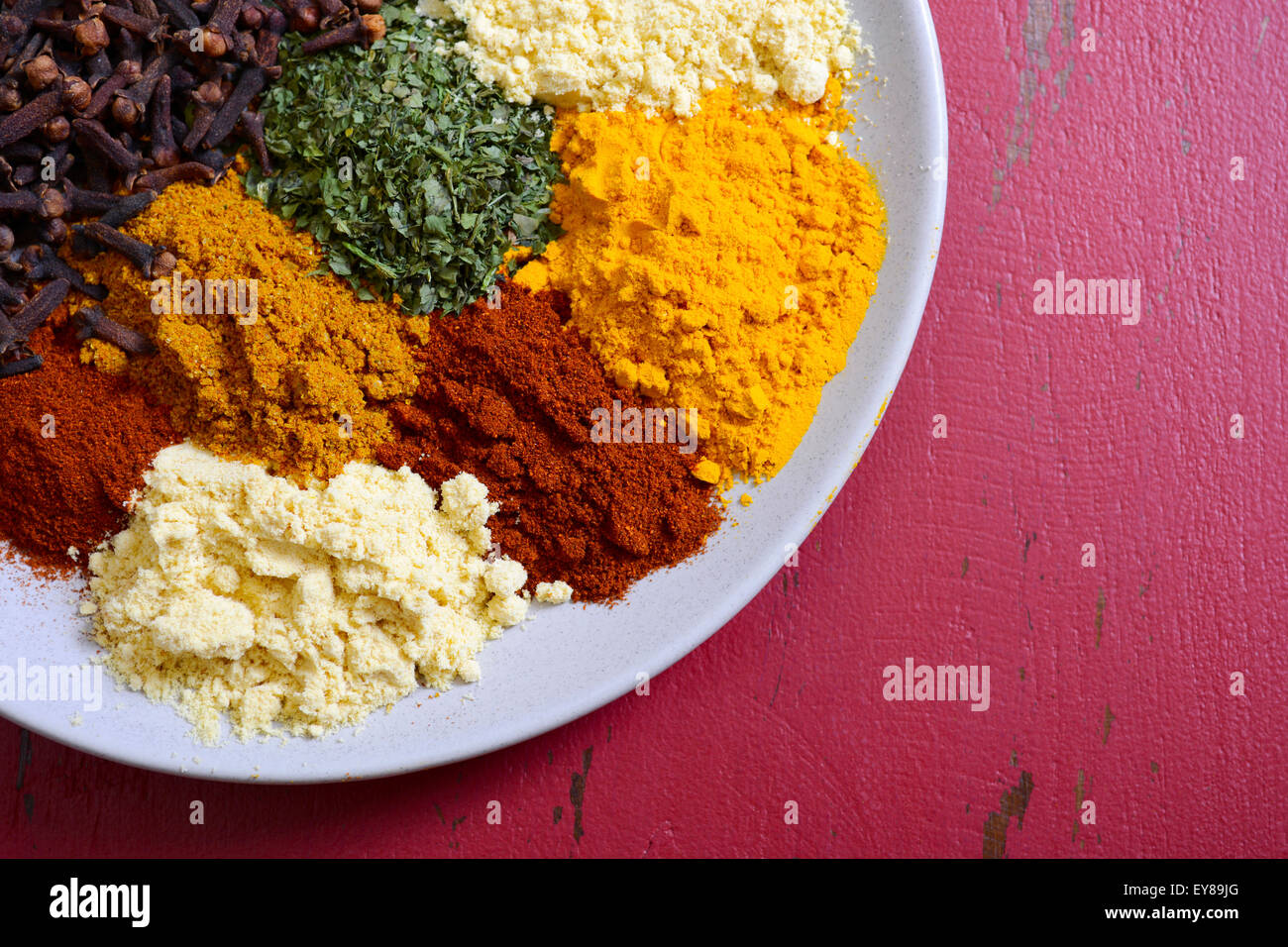Colorful cooking spices and herbs on round plate on vintage red wood table. Stock Photo