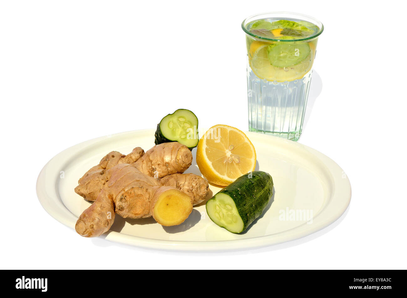 Glass of water with cucumber, lemon and ginger set on white plate Stock Photo