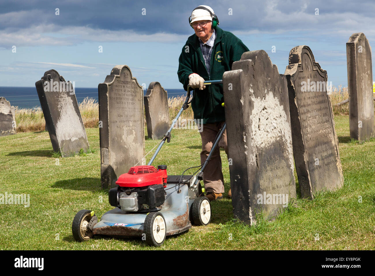 A man cutting the grass in the churchyard at St Mary's Church, Whitby, North Yorkshire, England, U.K. Stock Photo