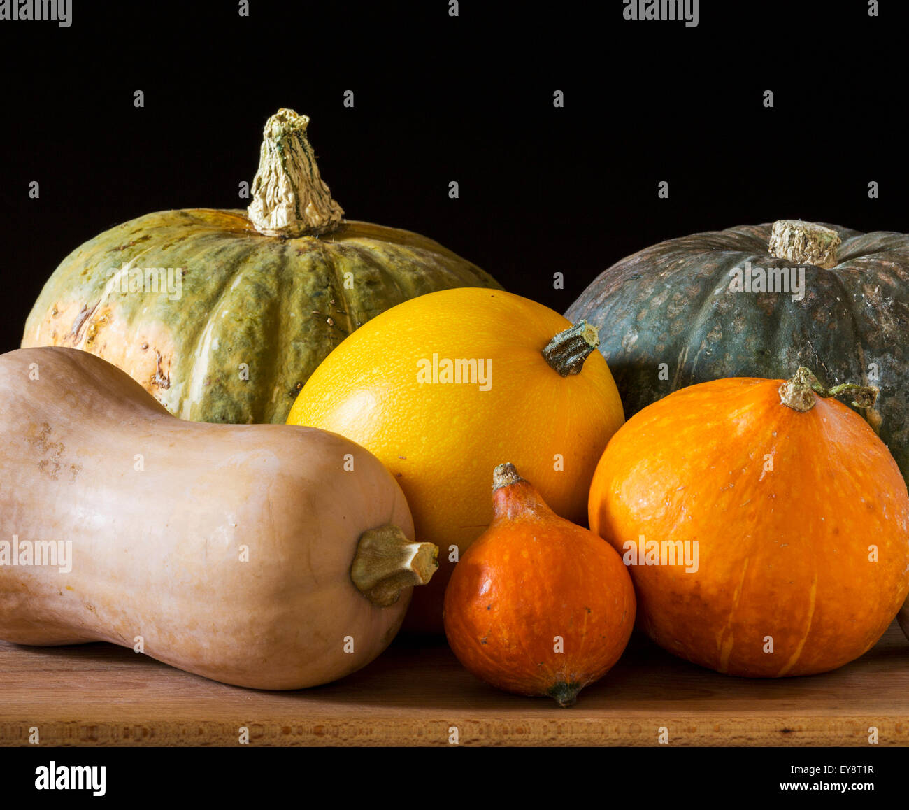 Close up of assorted colours and shapes of squash on a wooden board and black background; Calgary, Alberta, Canada Stock Photo
