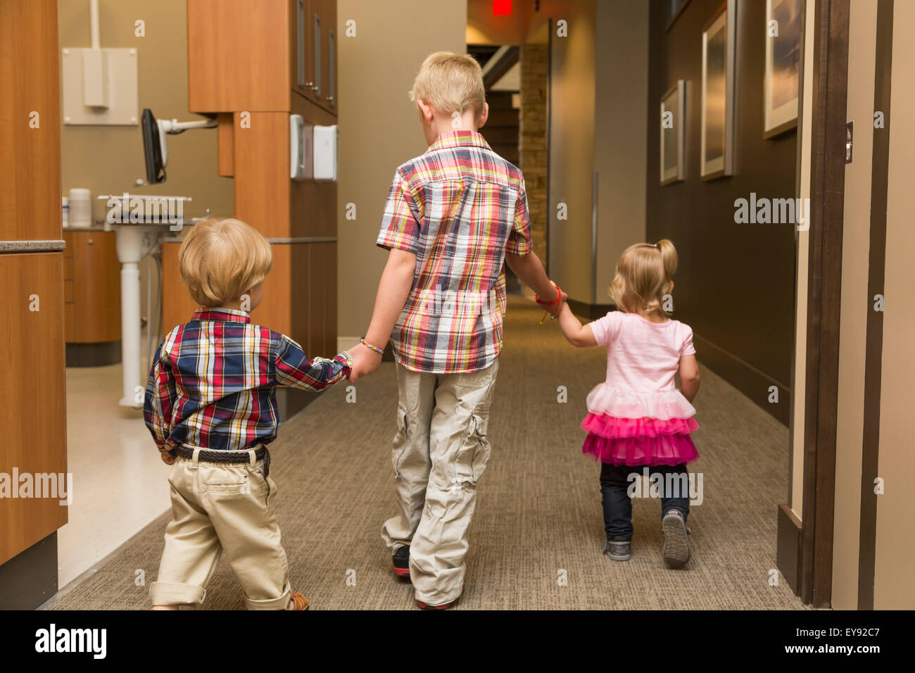Three young children holding hands and walking down hallway in family