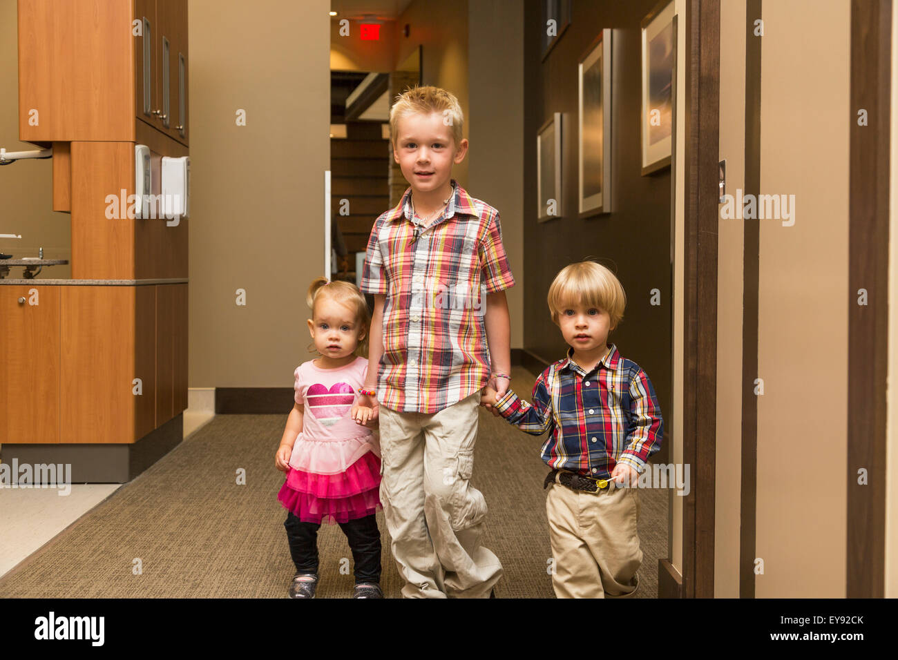 Three young children holding hands and walking down hallway in family
