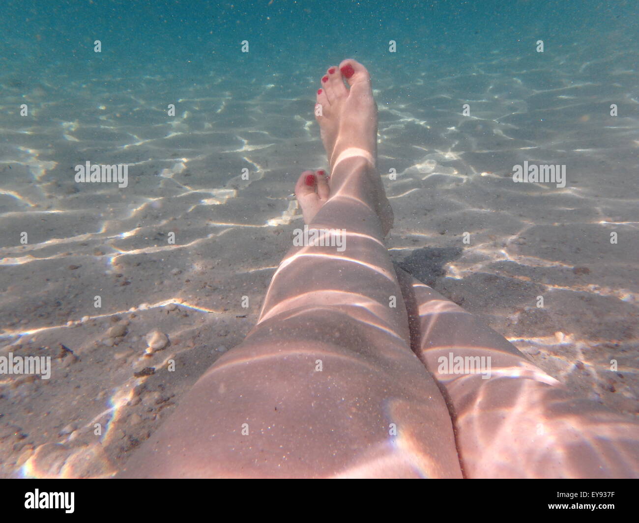 Woman enjoying the sea holding her feet with red nail polish at the bottom of the sea, underwater photography. Stock Photo