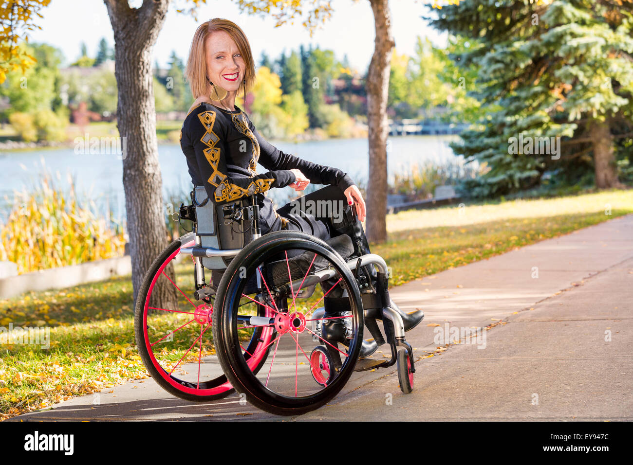 Young paraplegic woman in her wheelchair on a path in a city park in autumn; Edmonton, Alberta