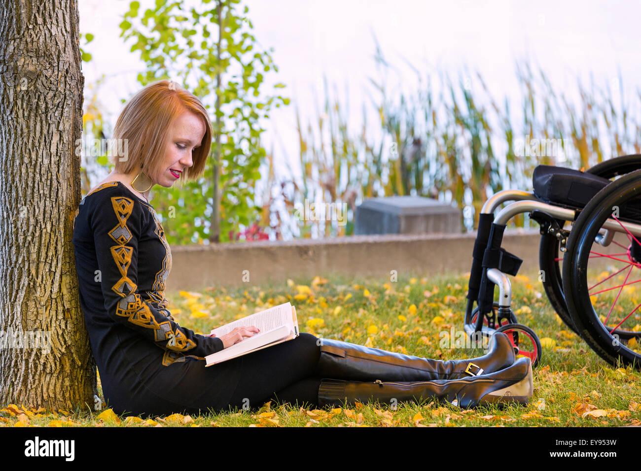 Young disabled woman sitting beside her wheelchair reading a book in a