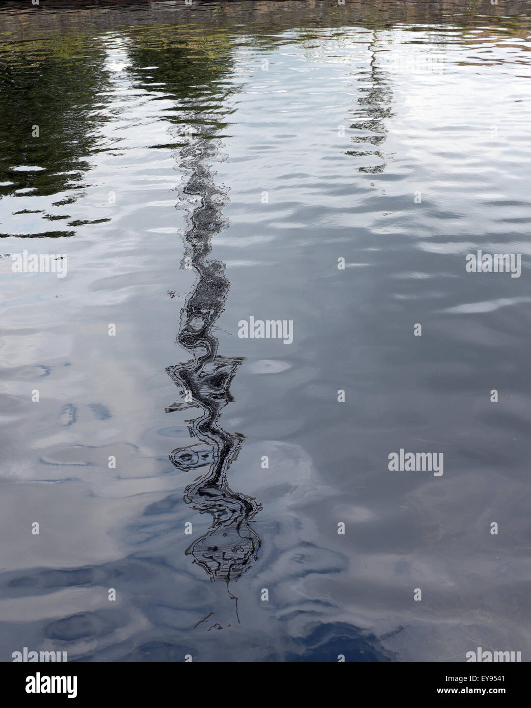 reflection in water of a simple straight pole results in a complex wavy line. Stock Photo