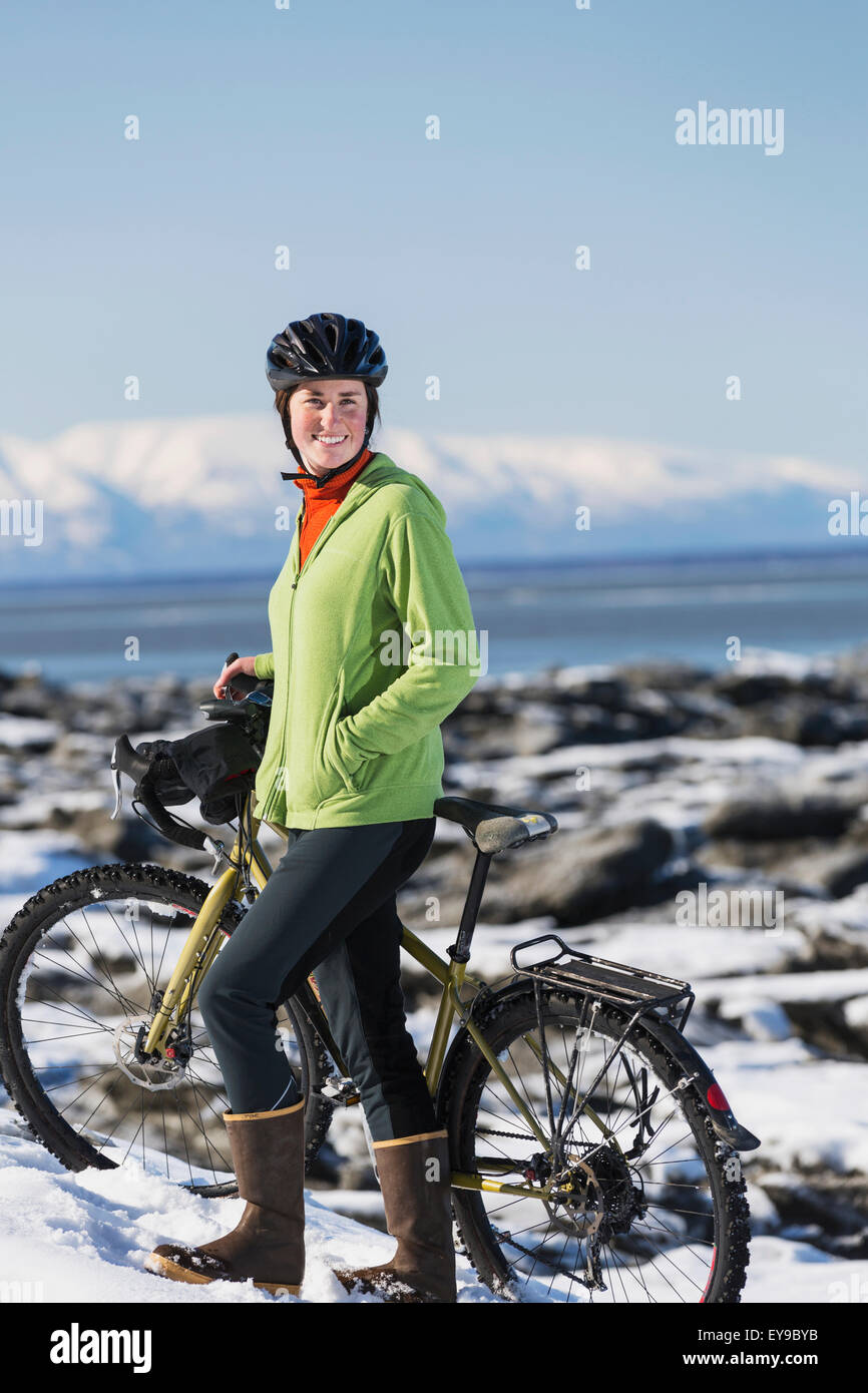 Young woman with her bicycle stands on frozen ice chunks along the Tony Knowles Coastal Trail, Anchorage, Southcentral Alaska Stock Photo