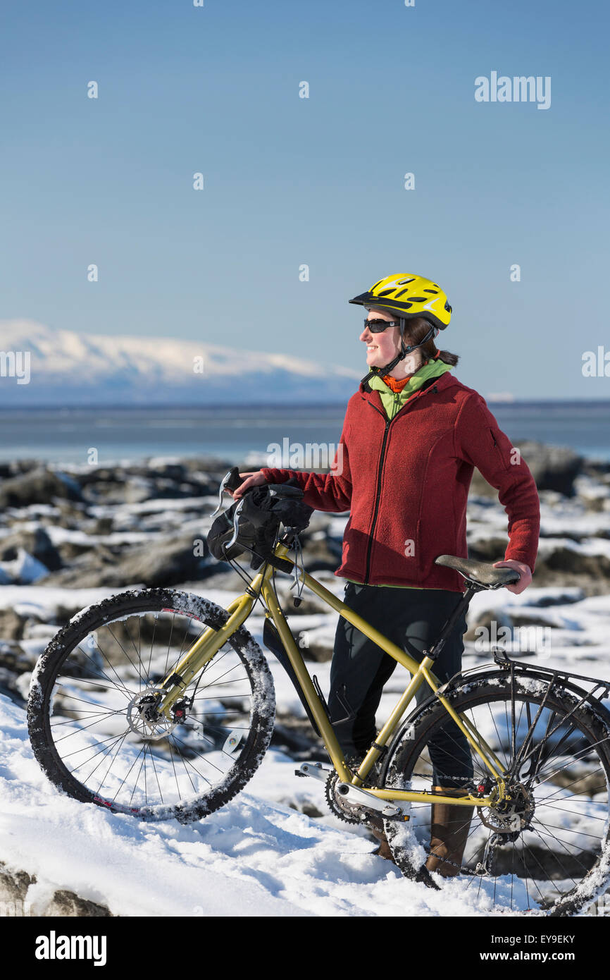 Young woman with her bicycle stands on frozen ice chunks along the Tony Knowles Coastal Trail, Anchorage, Southcentral Alaska Stock Photo