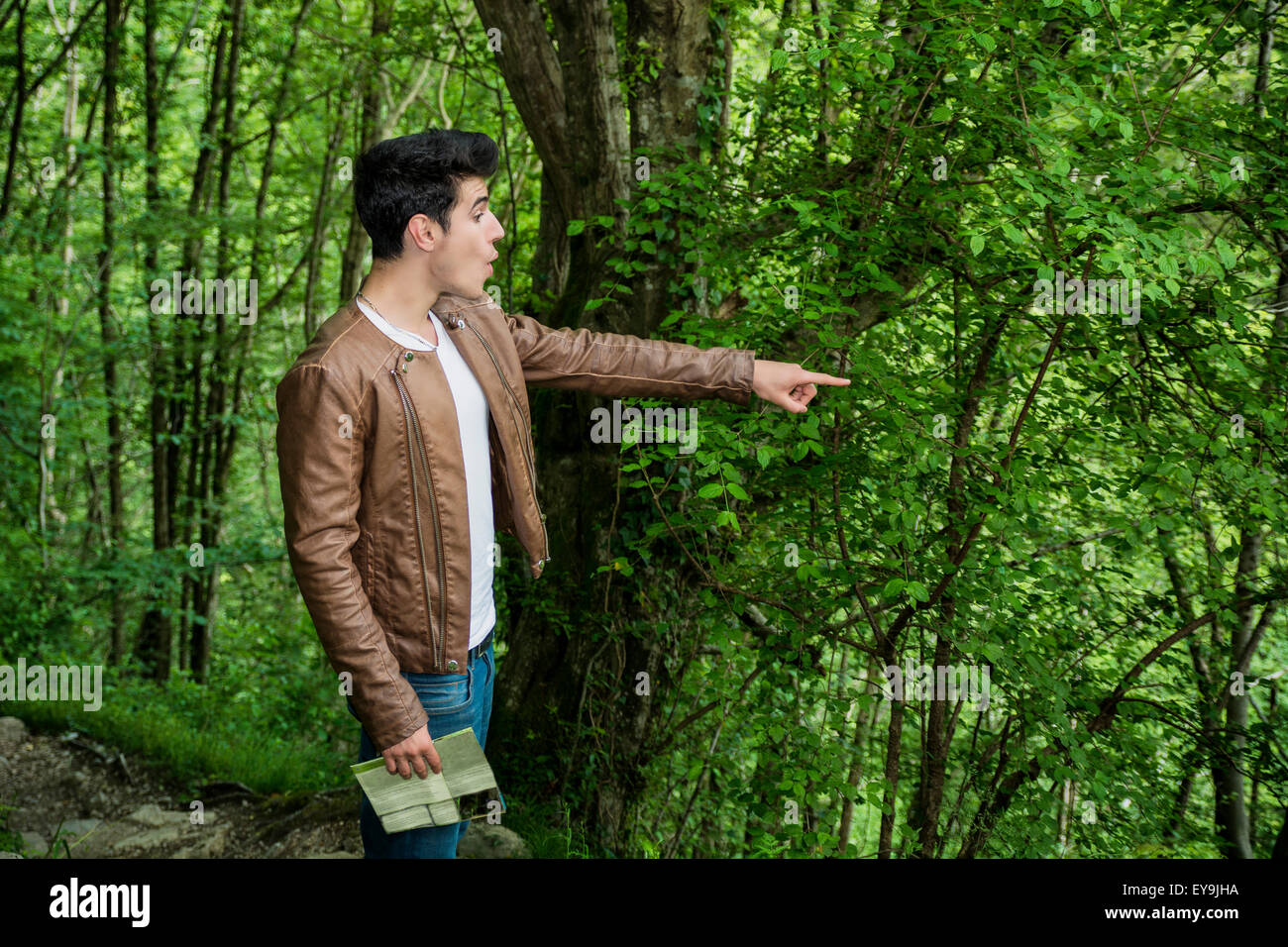 Astonished Looking Young Man Pointing into Distance in Wooded Area, Looking at Something Amazing While on Hike Through Forest Stock Photo