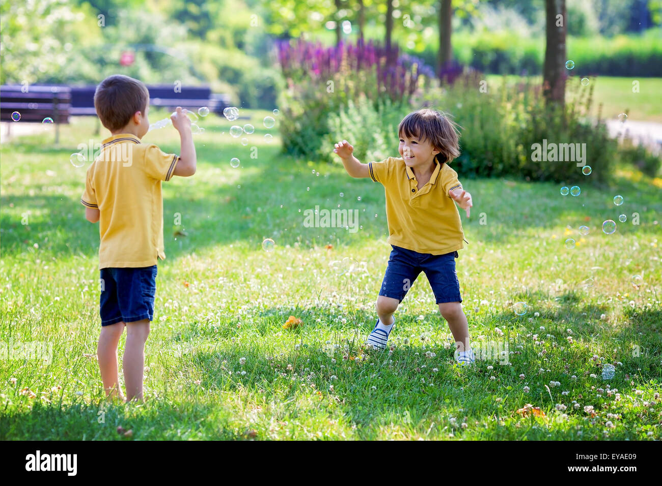 Two children in the park blowing and chasing soap bubbles and having fun, summer sunny day Stock Photo