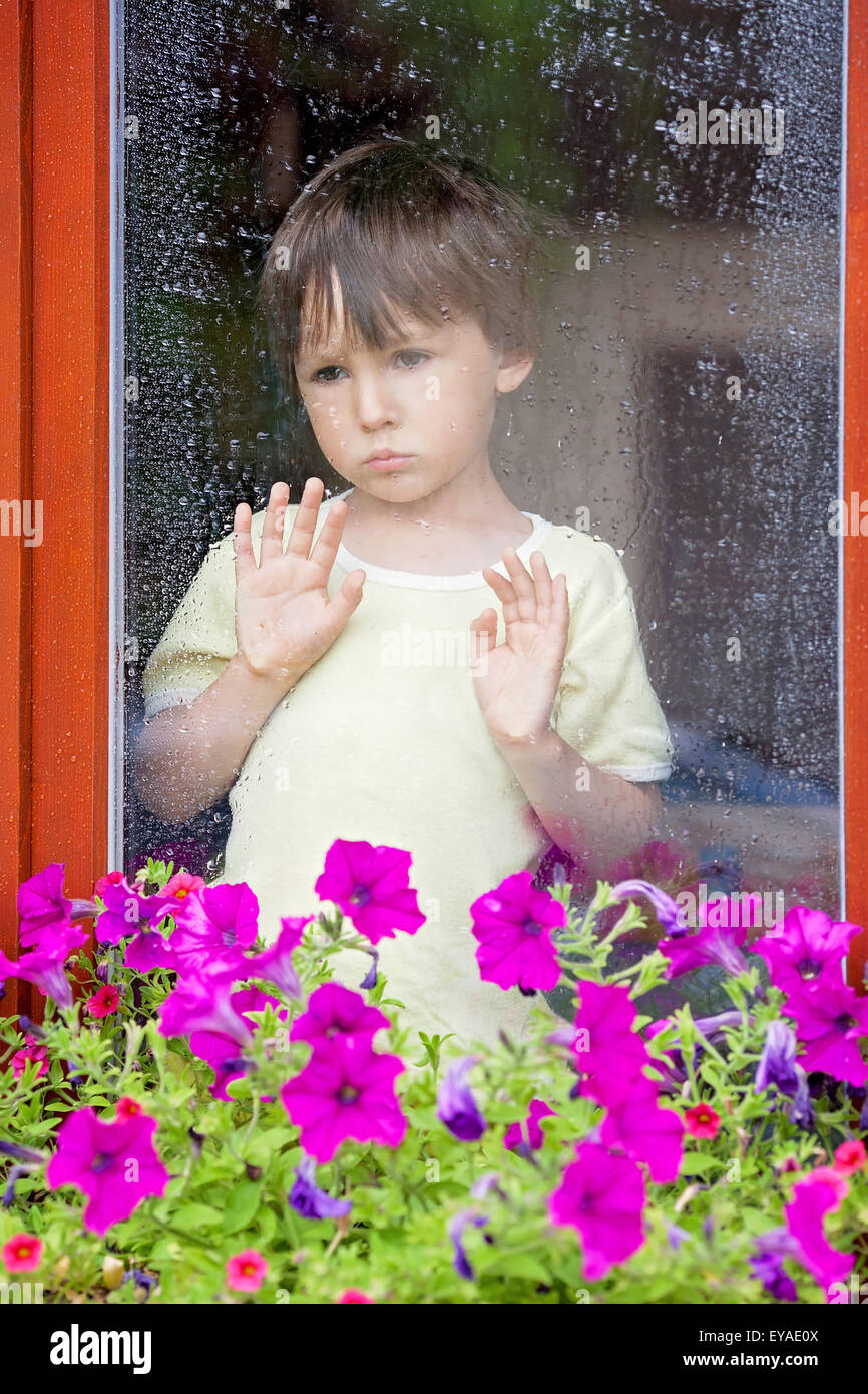 Little boy behind the window in the rain, looking sad Stock Photo - Alamy